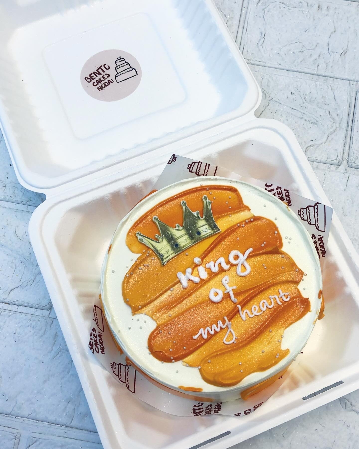 A bento cake is designed with orange shades on cake ad a crown print on it...