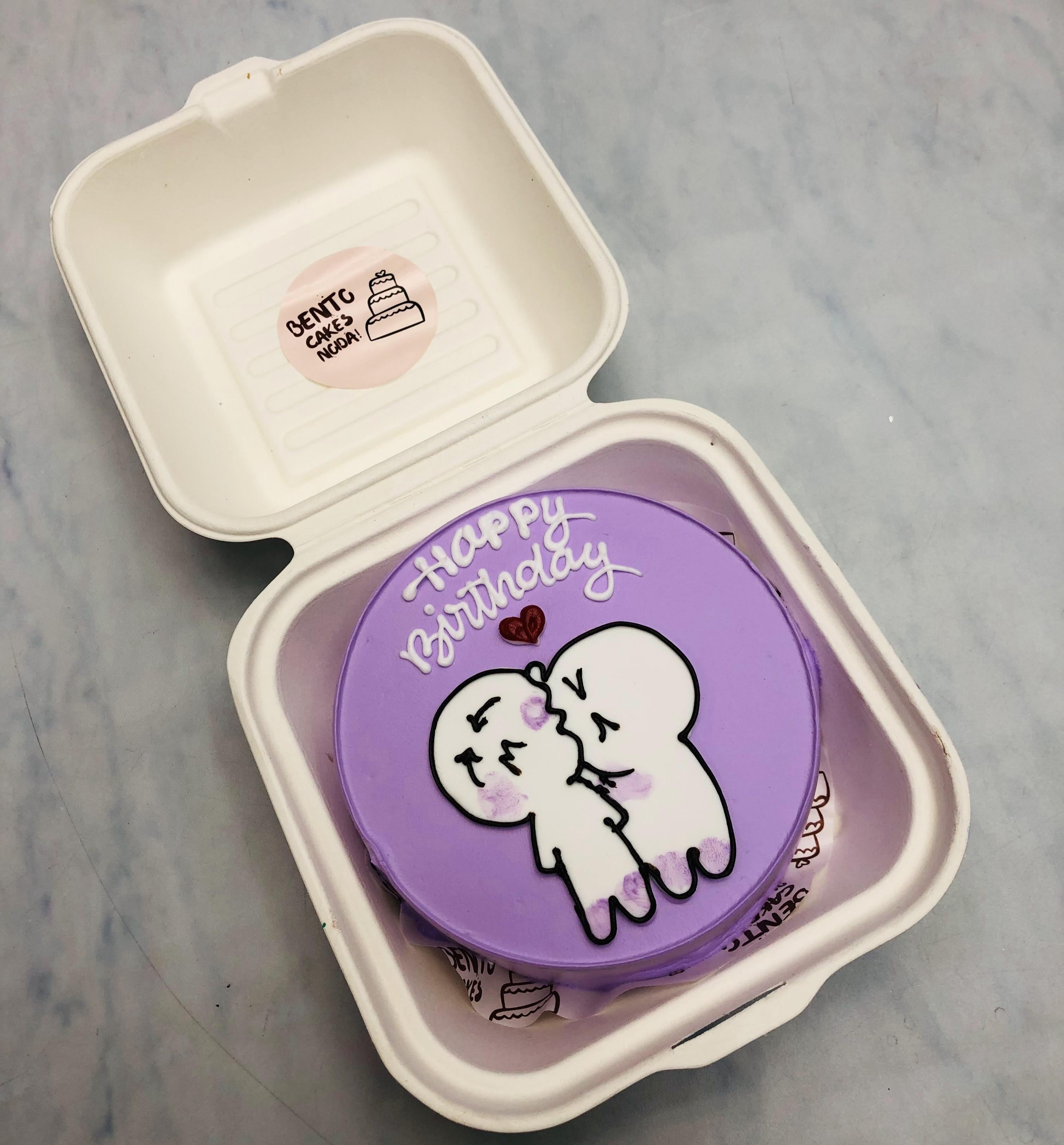 A kissing cartoon couple print ohn purple cake in a mini bento box.