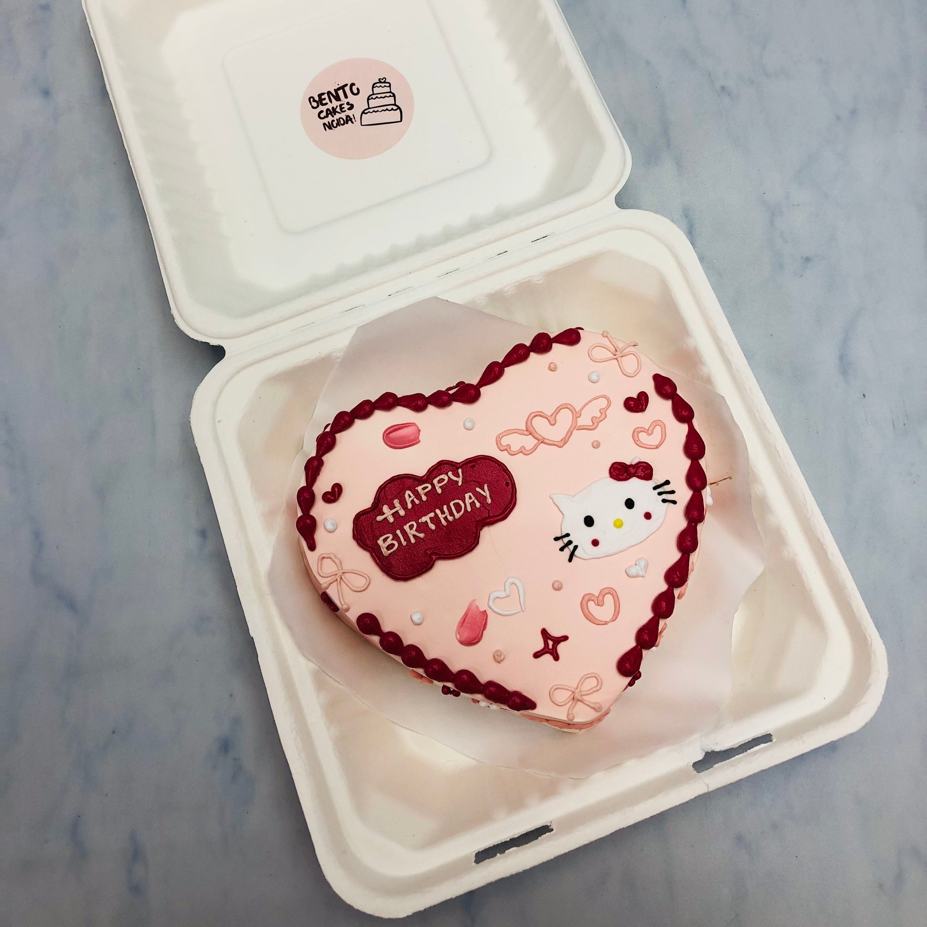 A peach color cake with dark red boundries and a kitty face design ion it.