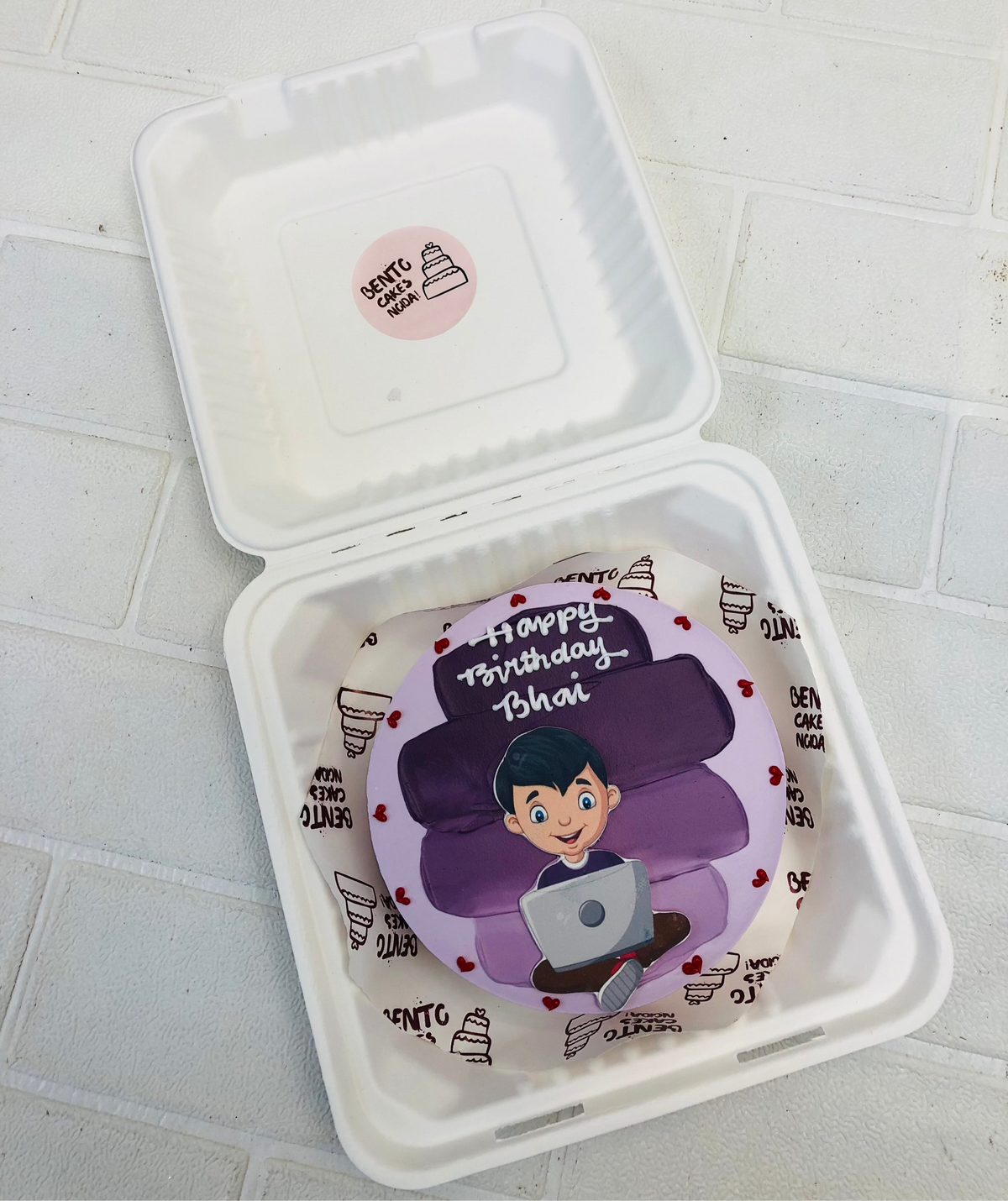 A purple shades on a purple bento cake having a men working on his laptop.