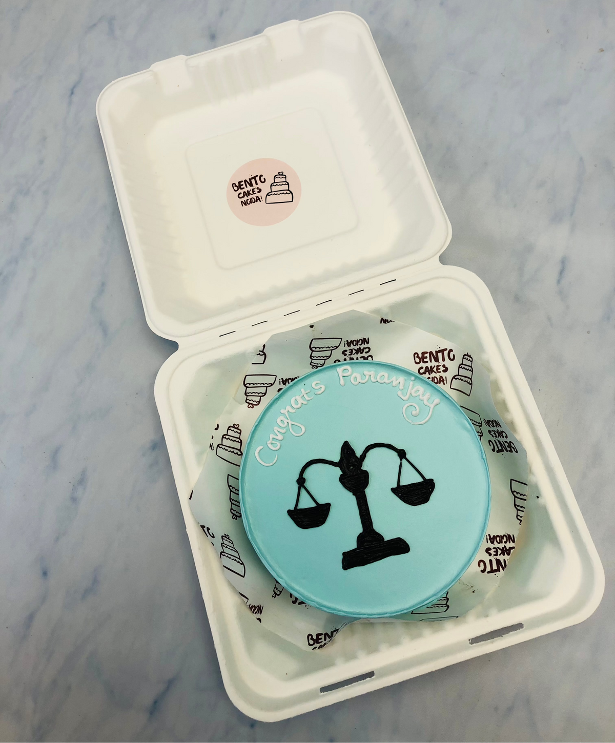 A light blue bento cake is designed for a men joined juduciary and having a law theme.