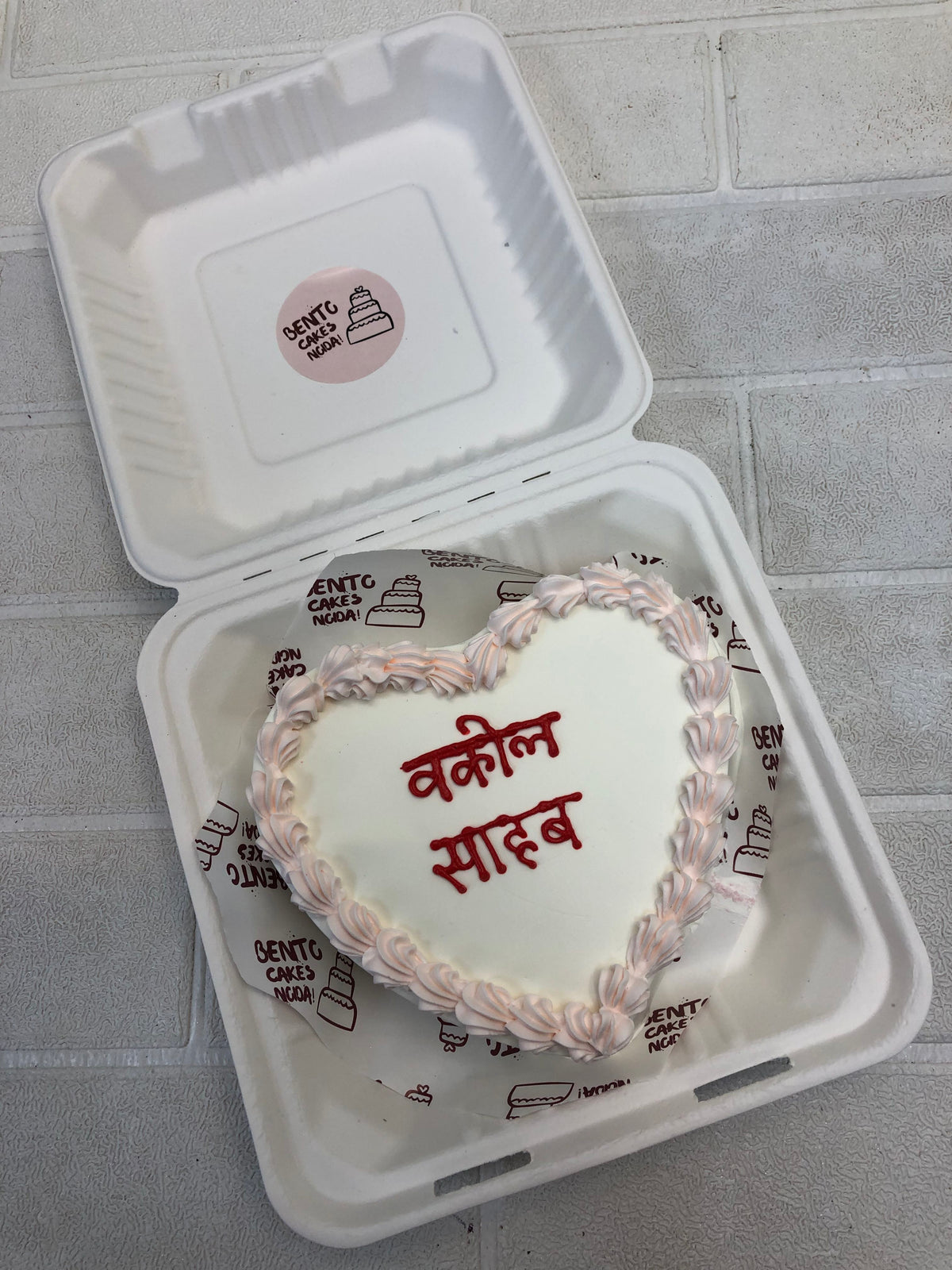 A white heart shape cake with baby pink bounday and a text written with red color.