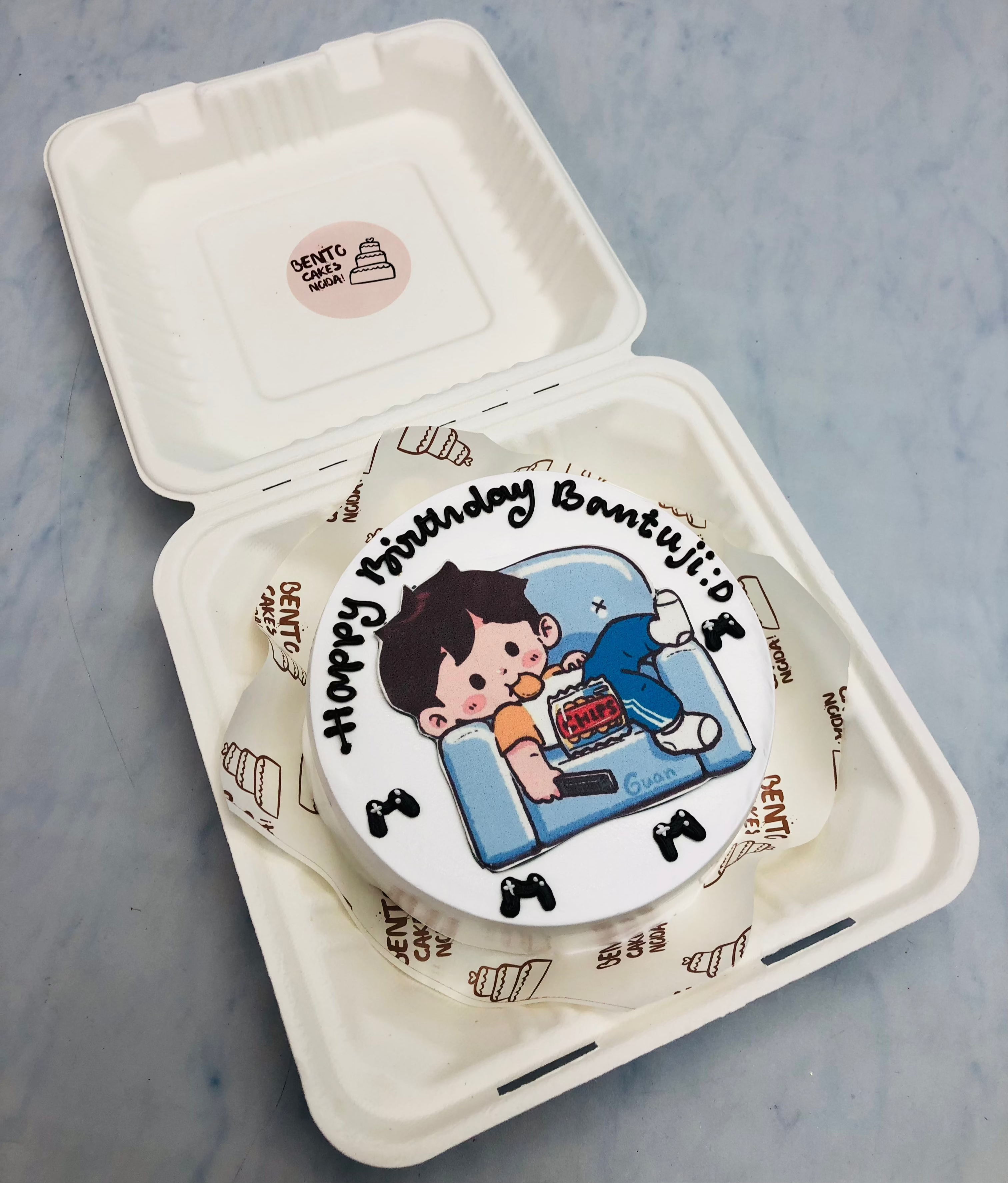 A boy lying on sofa and eating chips on his birthday, theme rinted on white bento cake.