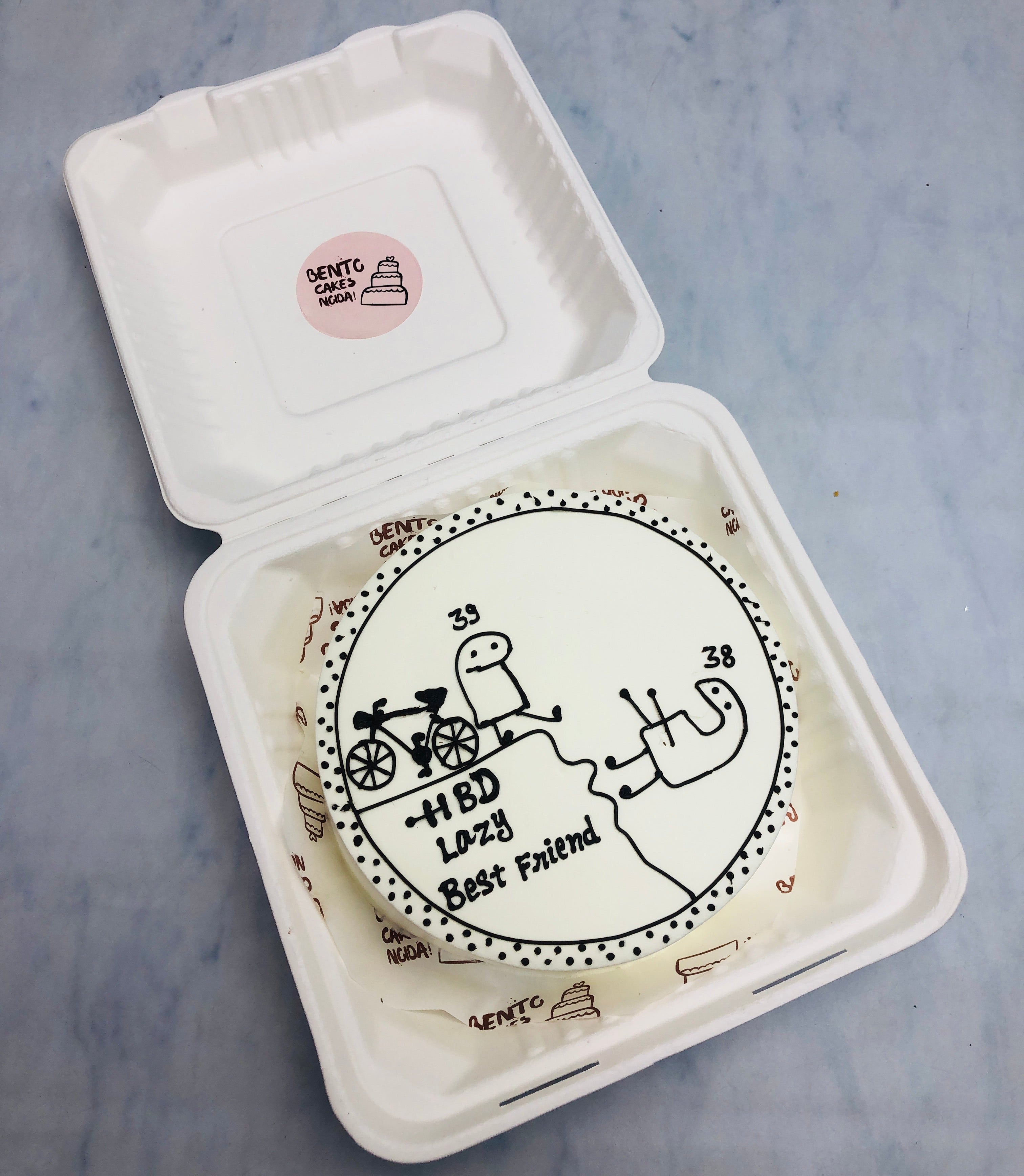 A white bento cake showing a lazy best friends birthday passing year from 38 to 39.