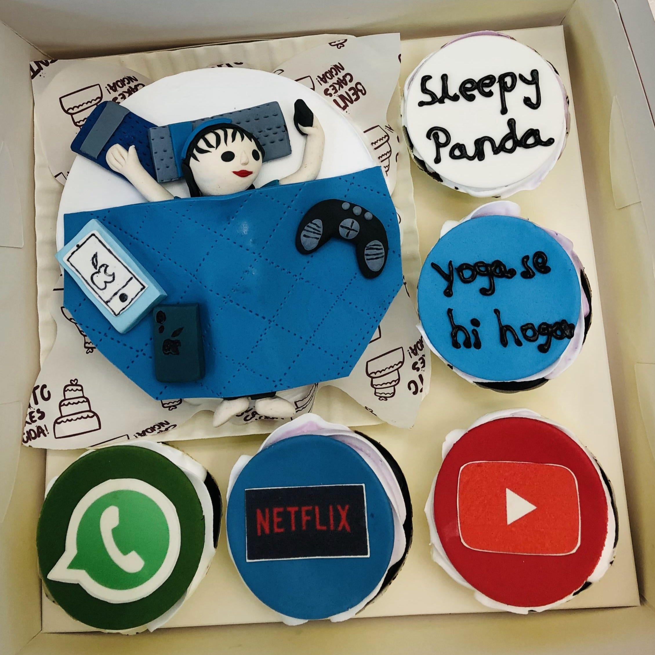 A bento combo having a round cake and 5 cupcakes set with different designs. Cake designed with a sleepy fondant girl having joystick, a cupcake having WhatsApp logo, another have Netflix logo, You Tube logo and two other having different text messages.