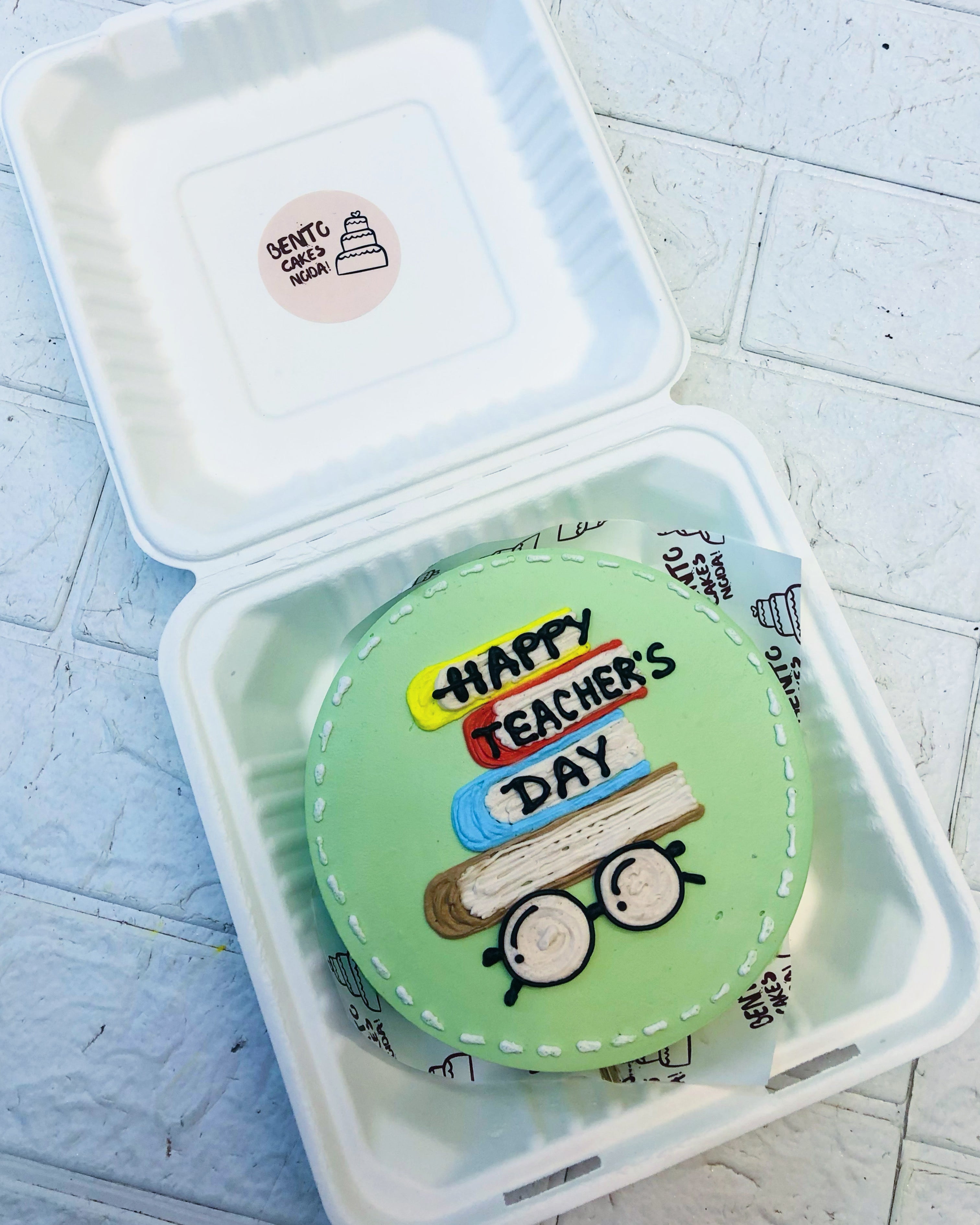 A light green bento cake is designed for techers day occasion with books and goggles design.