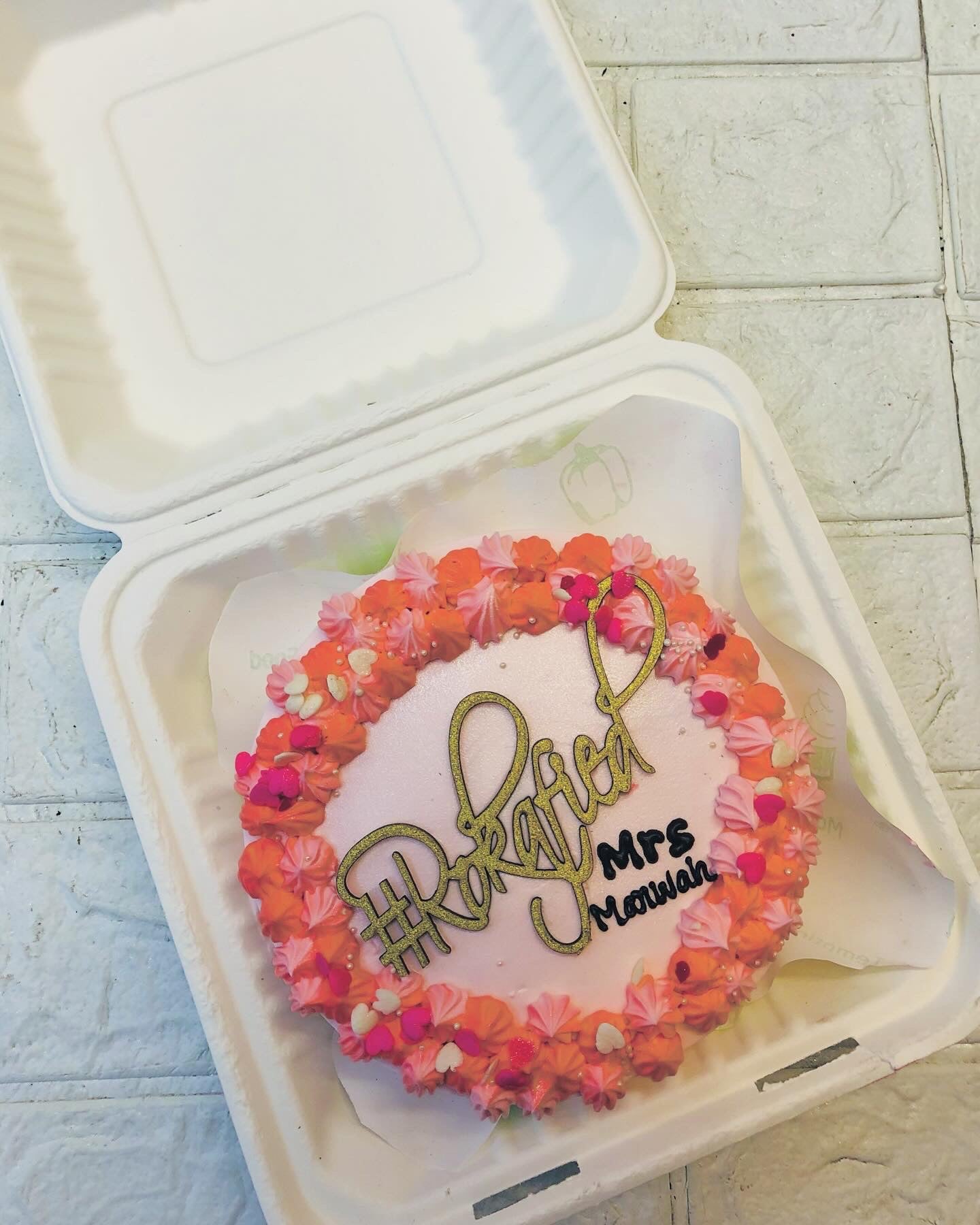 A light pink bento cake with orange-pink truffle design on it's boundary and a Rokafied topper placed on it.