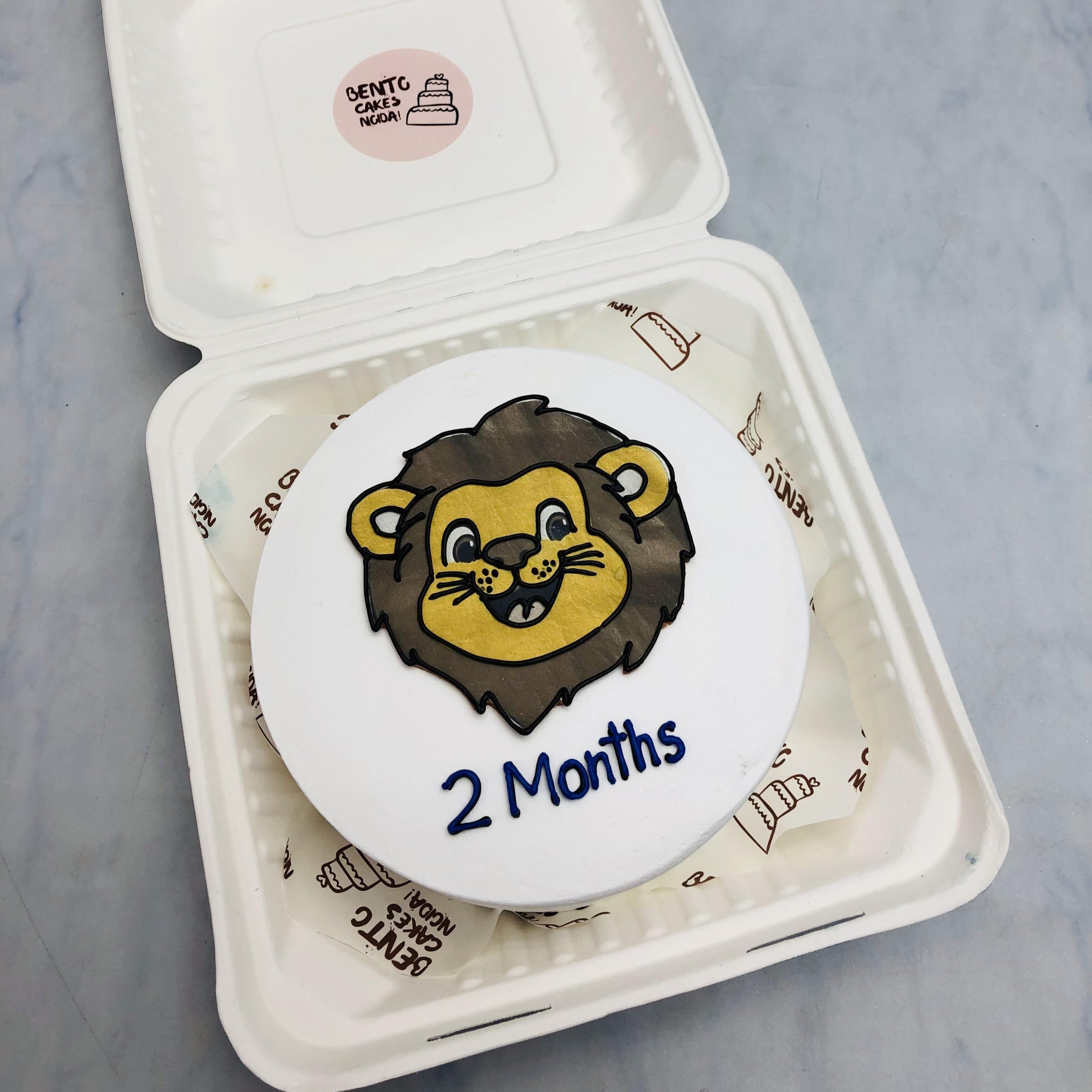 A white bento cake with cute lion face design for 2 months baby.