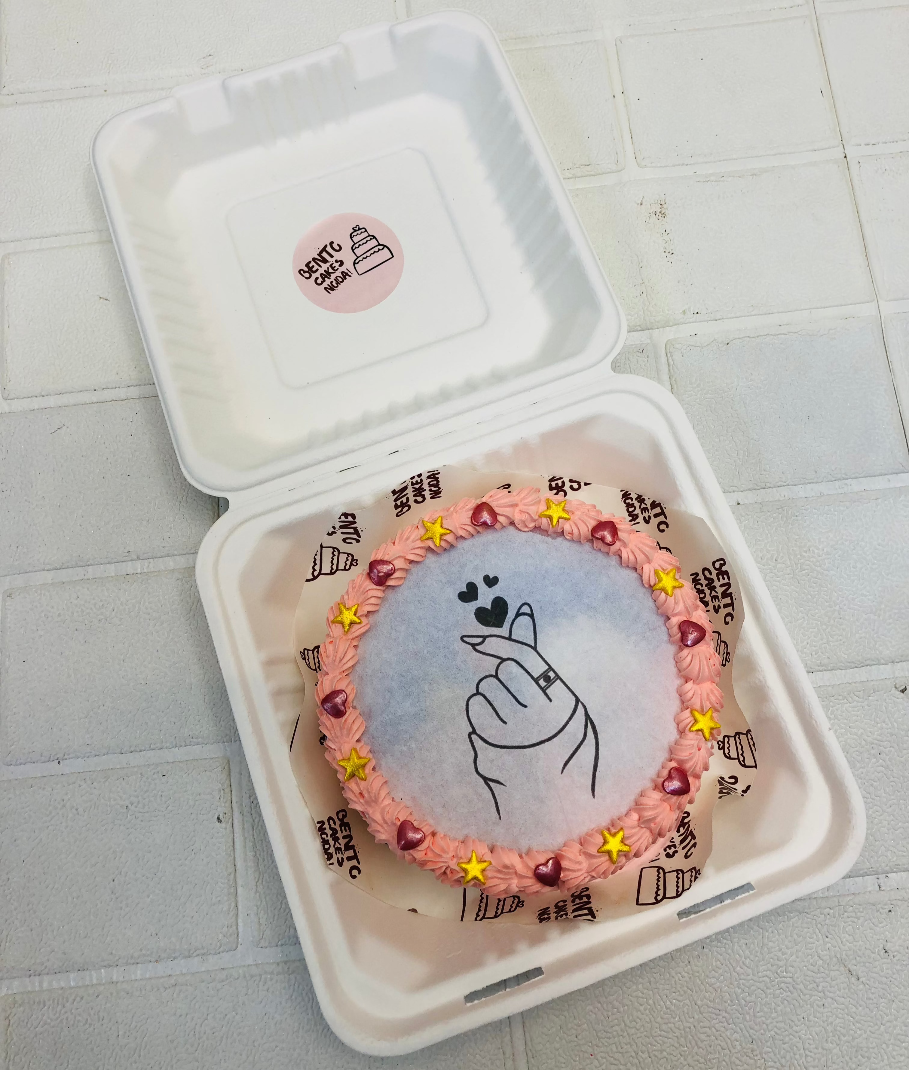 A rose gold color fire bento cake in round shape with love theme and decorated with golden stars and redb hearts.