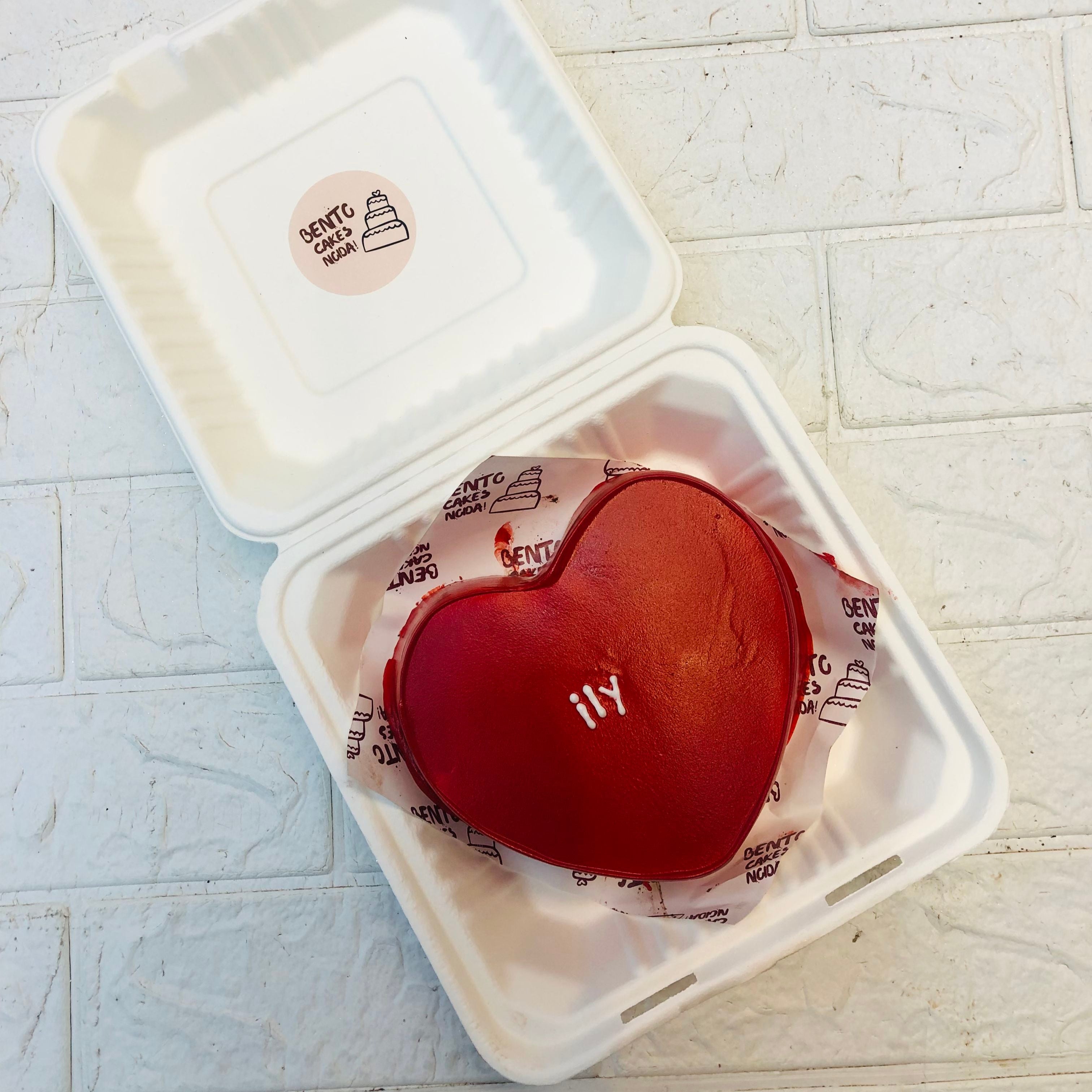 A dark red heart shape cake with a "ily" text on it.