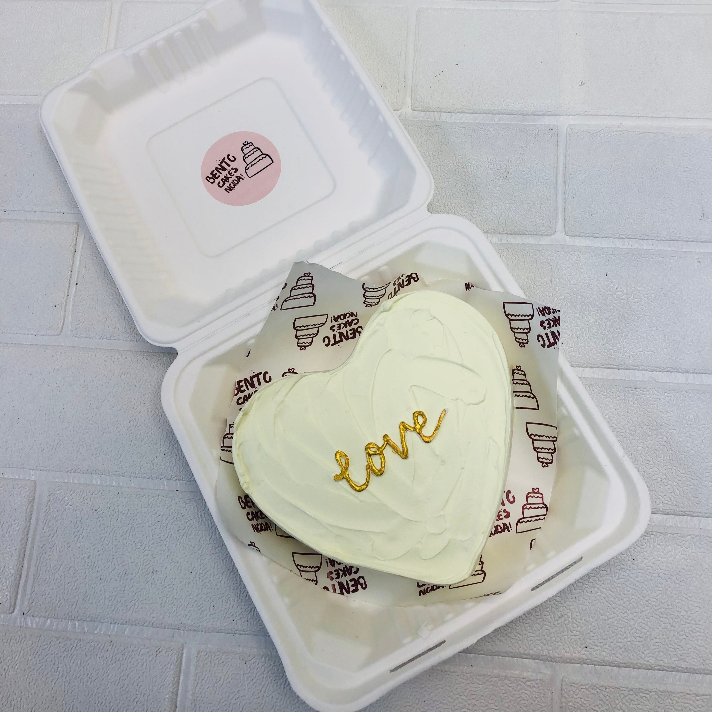 A white heart shape cake a golden text on it.