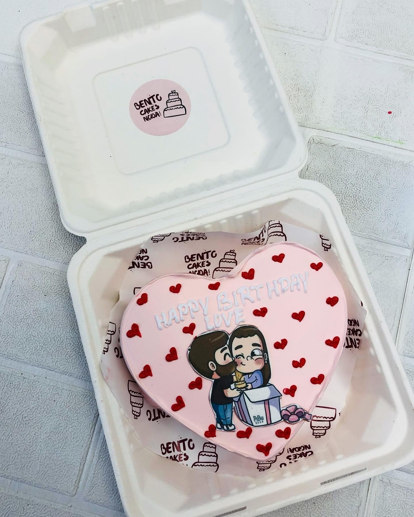 A light pink cake with kissing couple with red hearts.