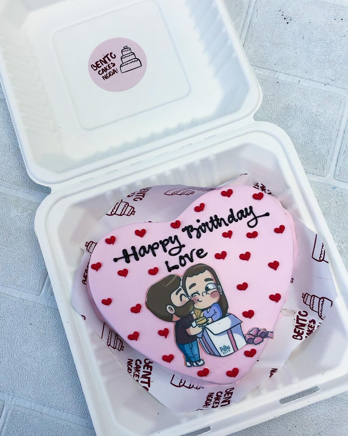 A heart-shaped cake featuring a photo of a couple, symbolizing love and celebration for a special occasion.
