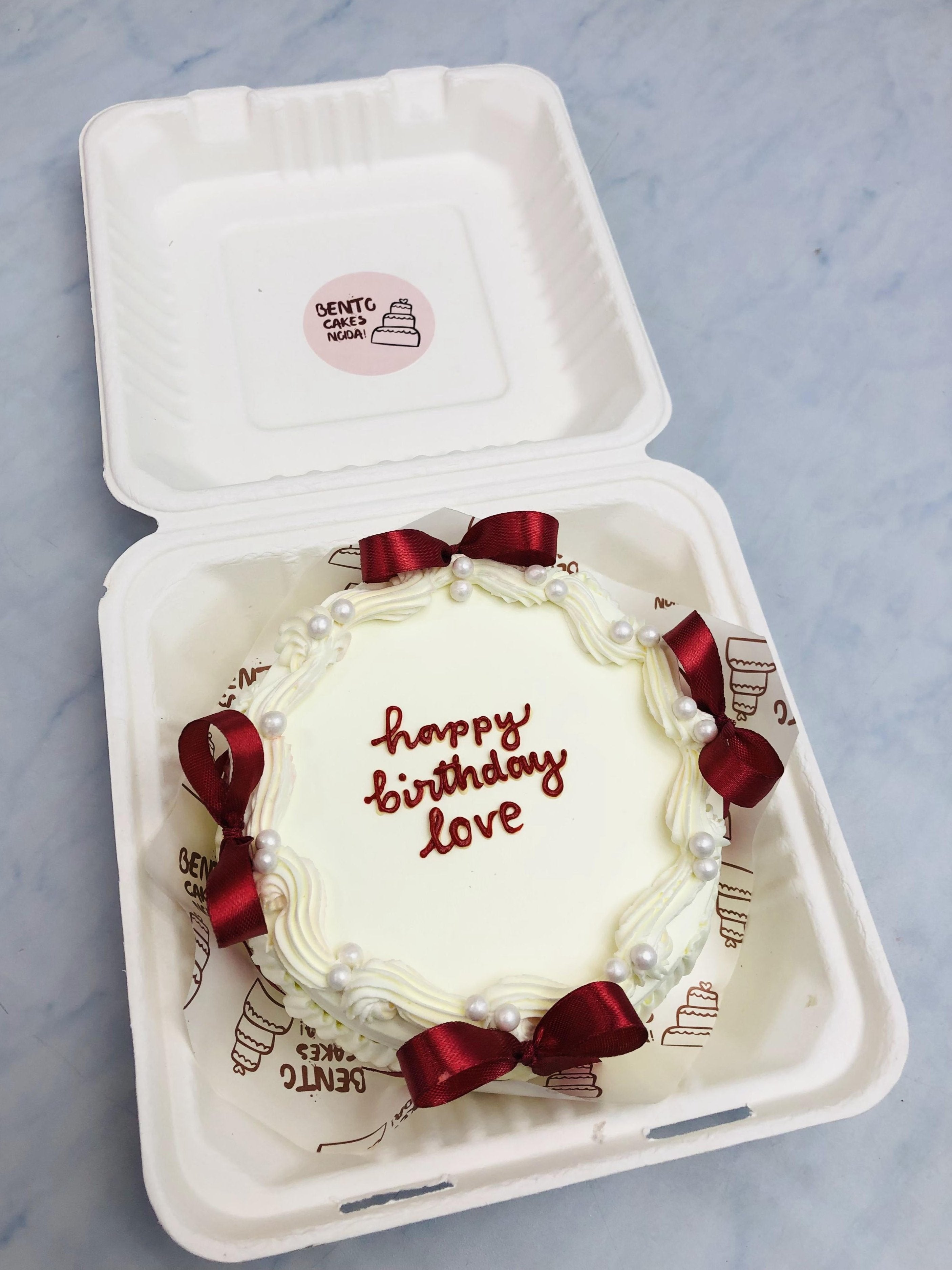 A designer white bento cake having red bows and decorated with white sprinkles.
