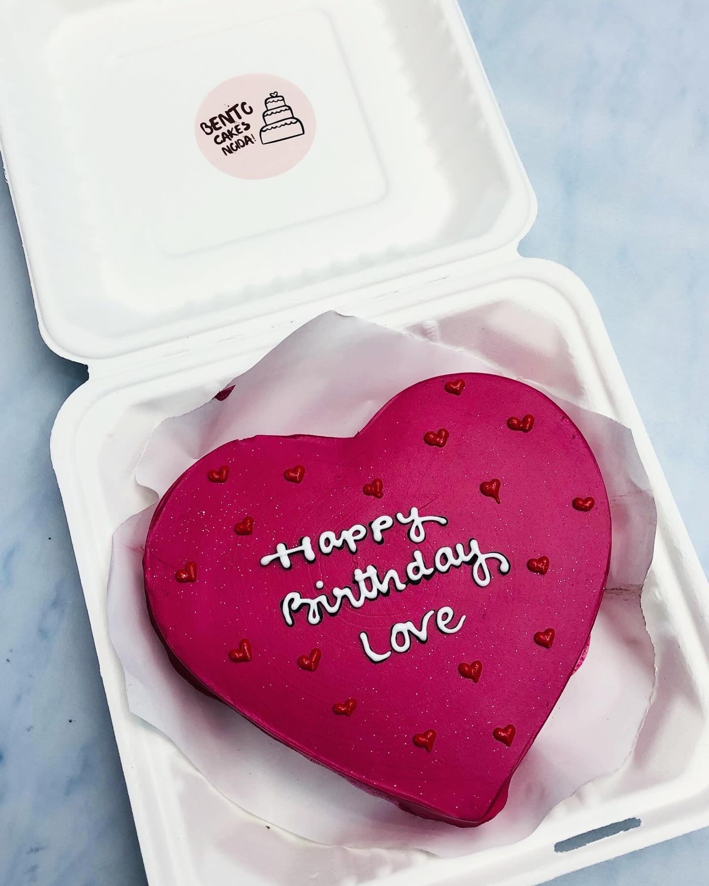 A dark pink icing cake with red little hearts design all over the cake and a text written with white icing.
