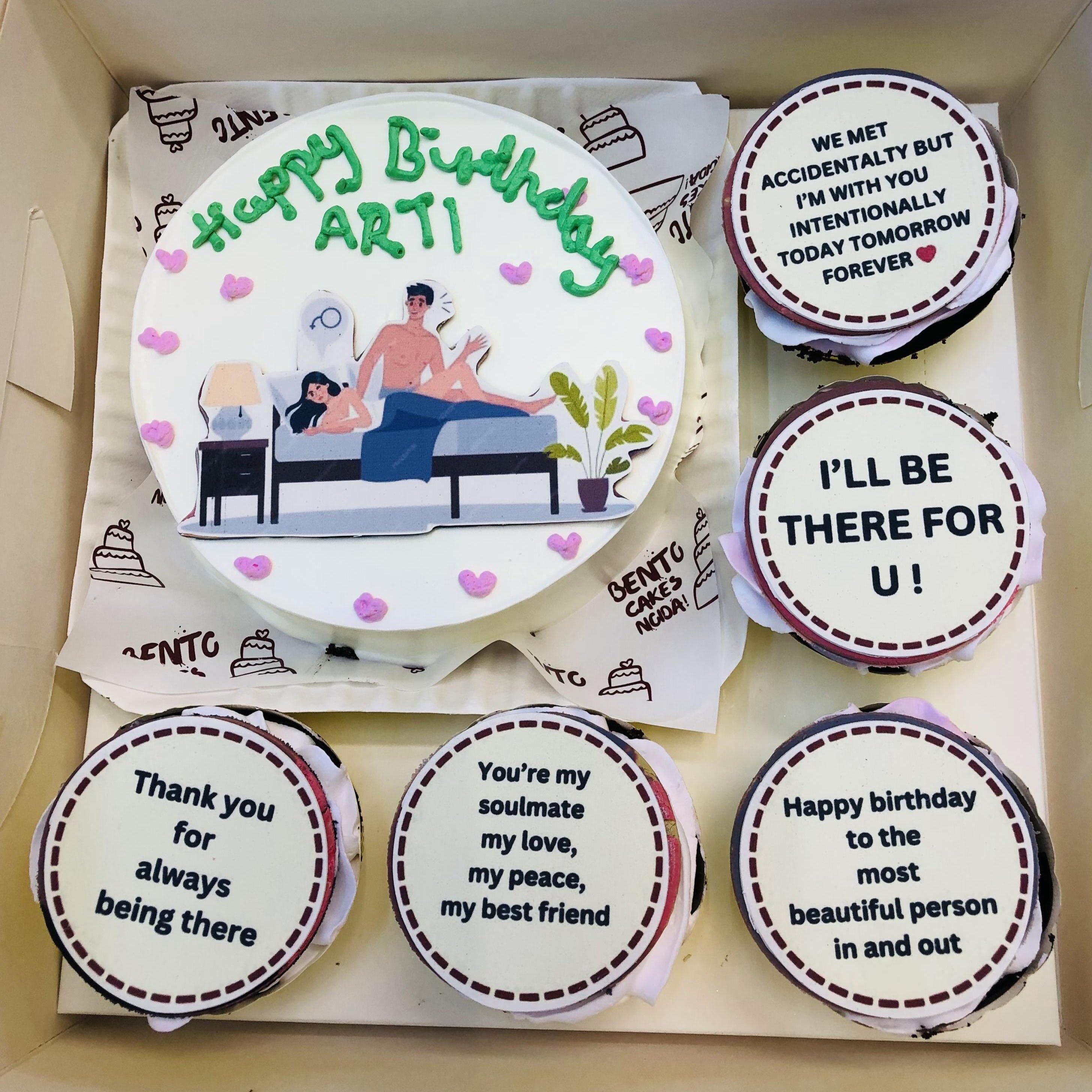 A "Loving Couple Bento Combo Cake" featuring a main cake with a depiction of a couple sitting on a bed, surrounded by pink heart decorations. The text "Happy Birthday ARTI" is written in green icing. Five accompanying cupcakes display heartfelt messages expressing love and gratitude.