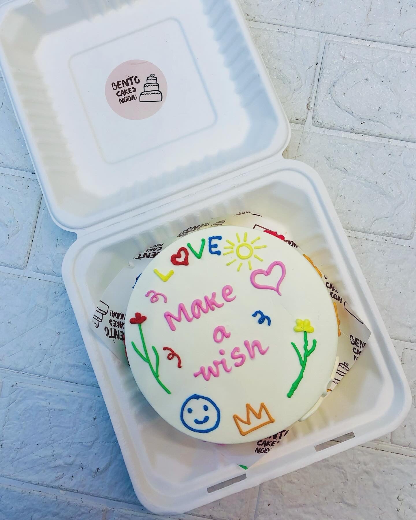A white bento cake designed with cute drawings and a "Make a wish" text written on it.