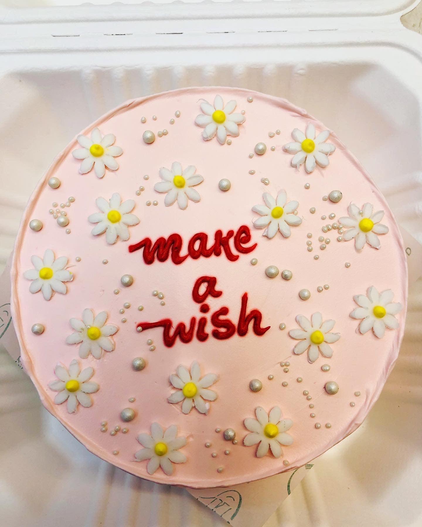 M rose gold cake is decorated with white florals design on its top and a text "make a wish" written with red color on it.