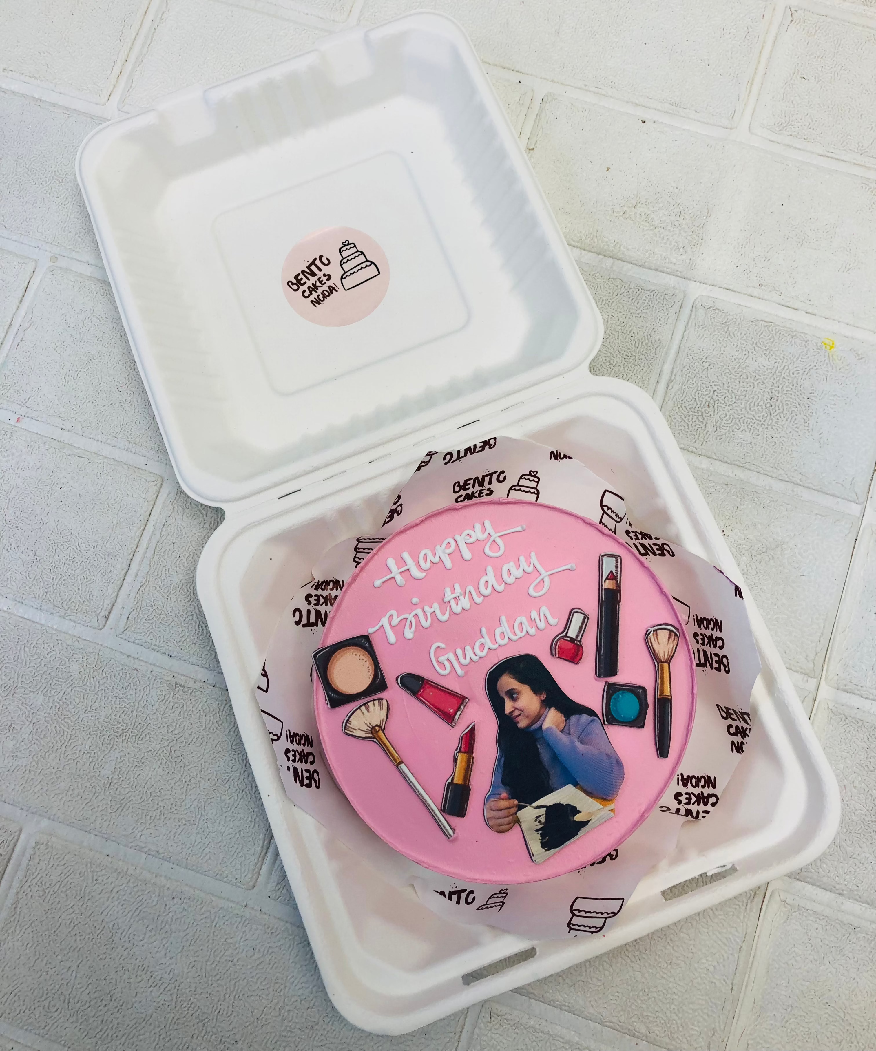 A light pink bento cake is designed with a birthday girl print with her make items.