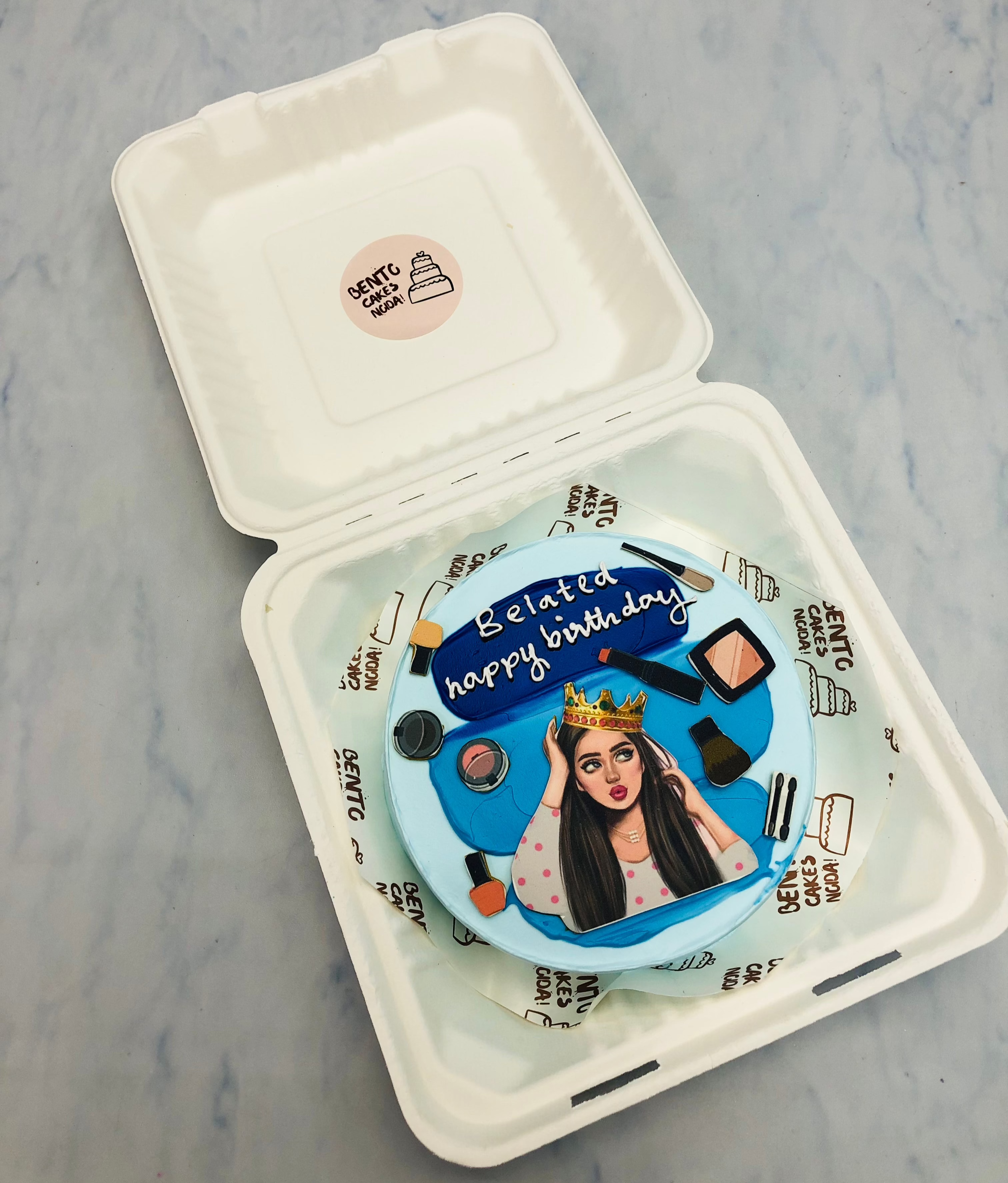 A light blue bento cake with a makeup queen with her makeup items.