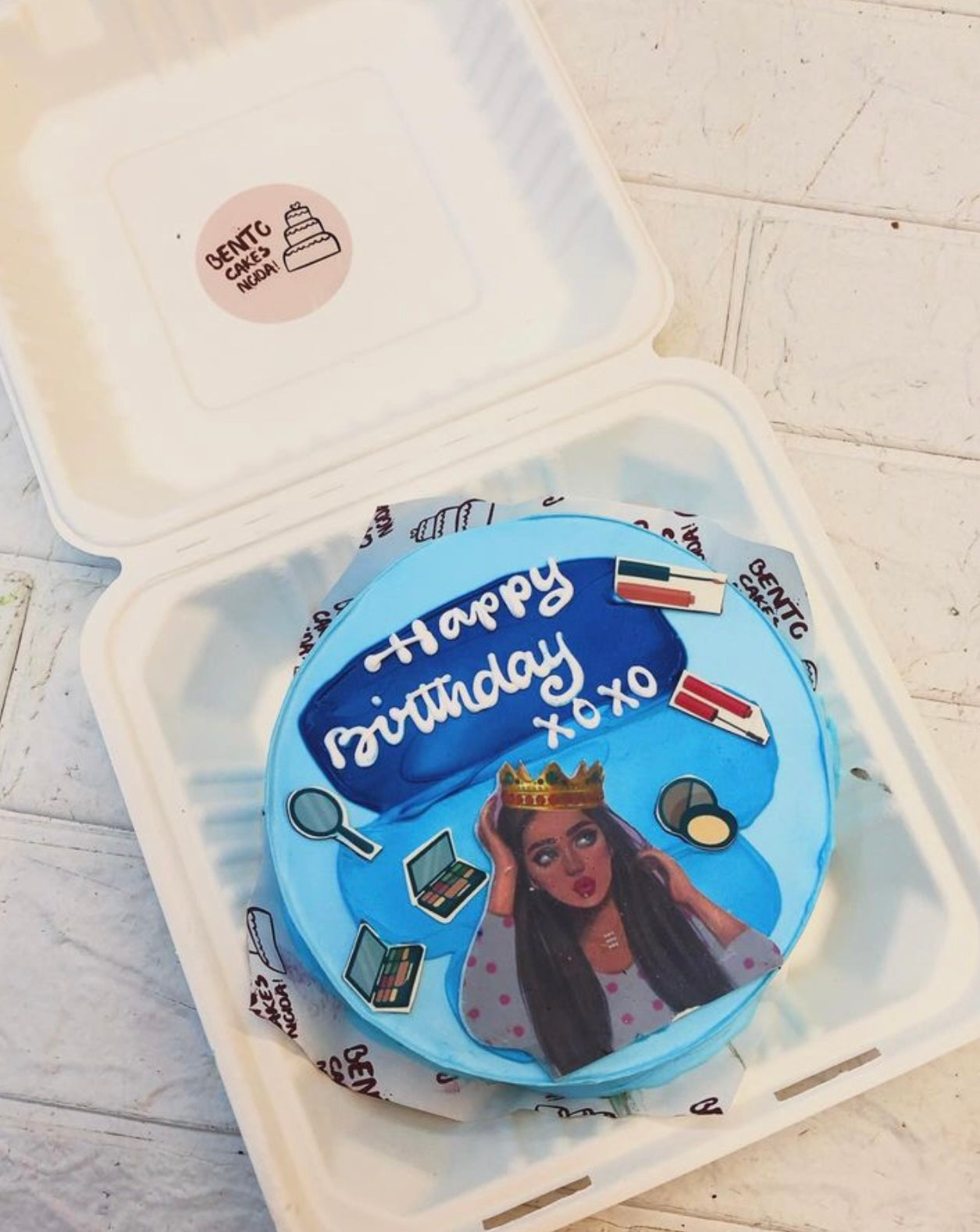 A blue bento cake having a makeup lover girl print with her makeup items.