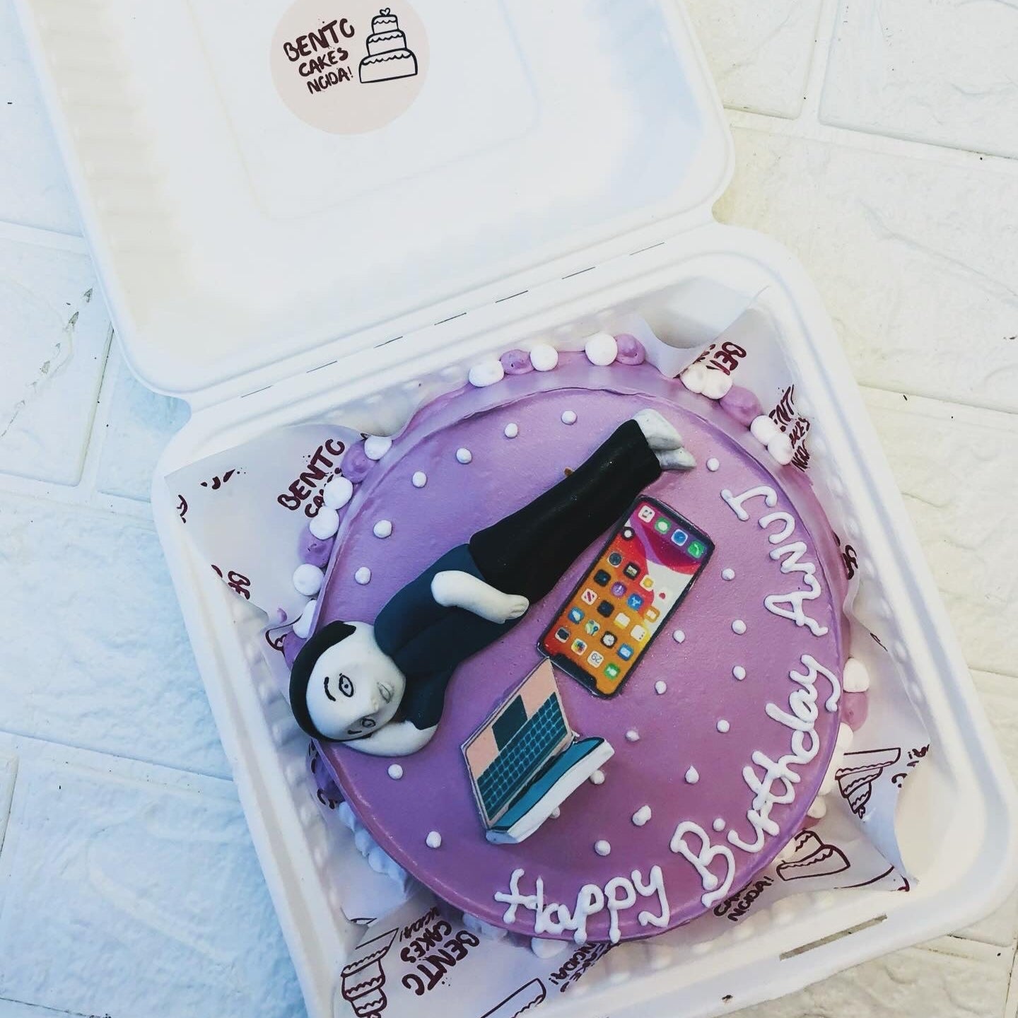 Purple color bento cake designed with a sleepy man on the top and some gadgets on it.