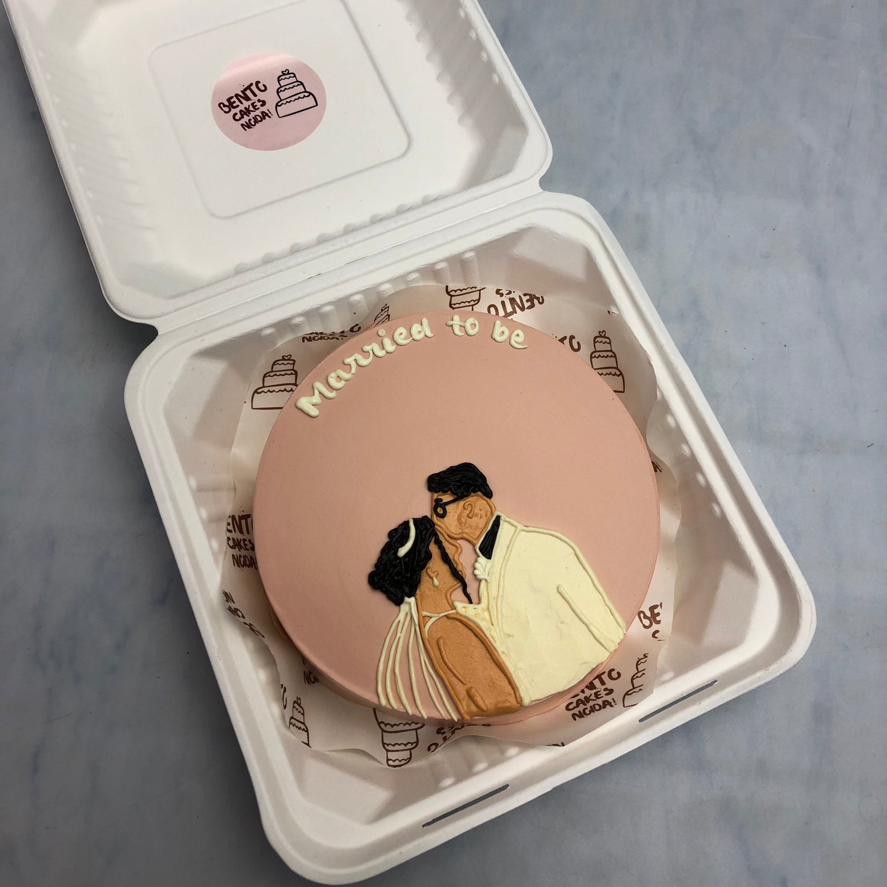 A light brown bento cake having a kissing couple drawing with a "Married to be" text.