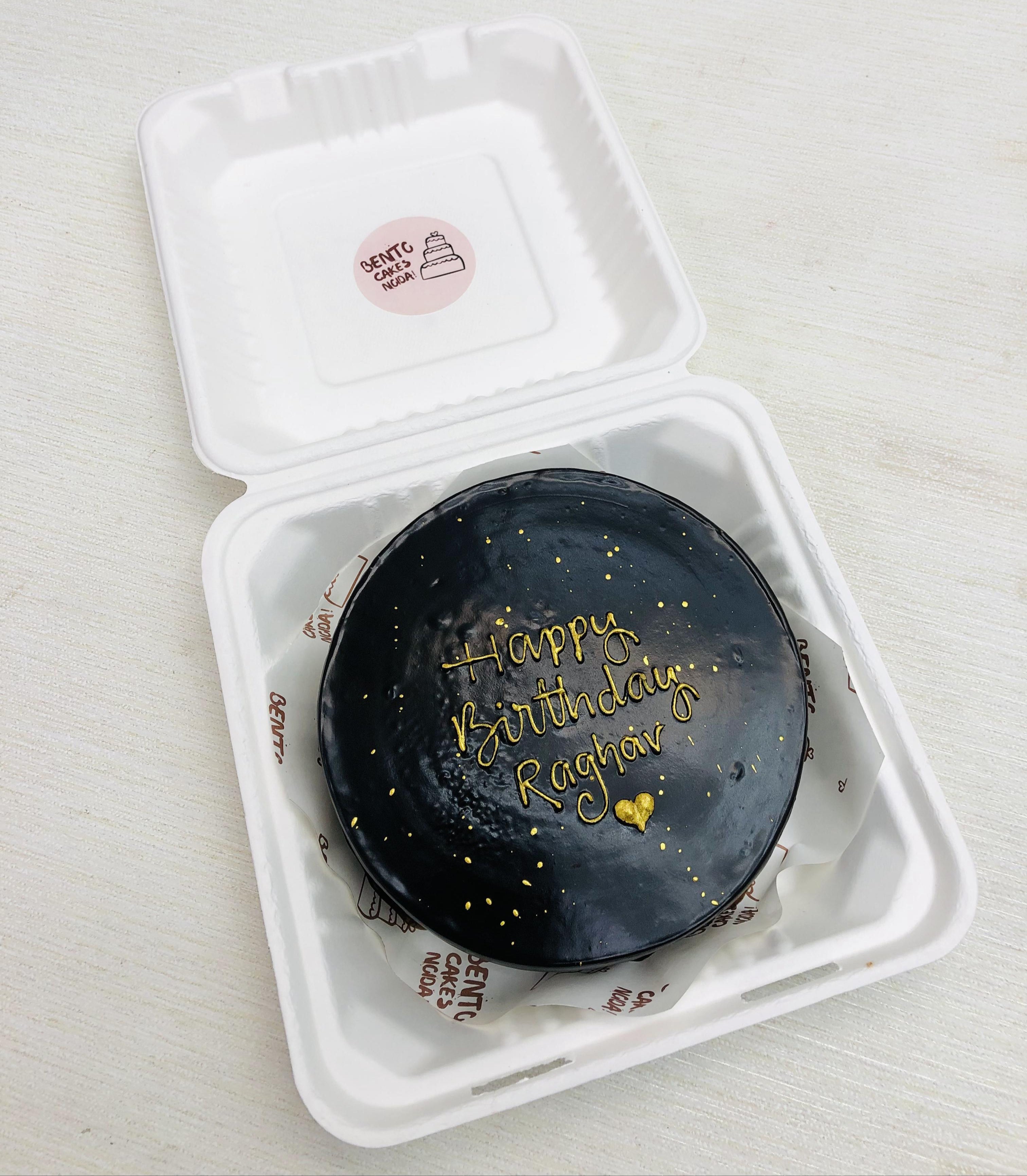 A dark chocolate bento cake having a golden heart with golden birthday wishing text.