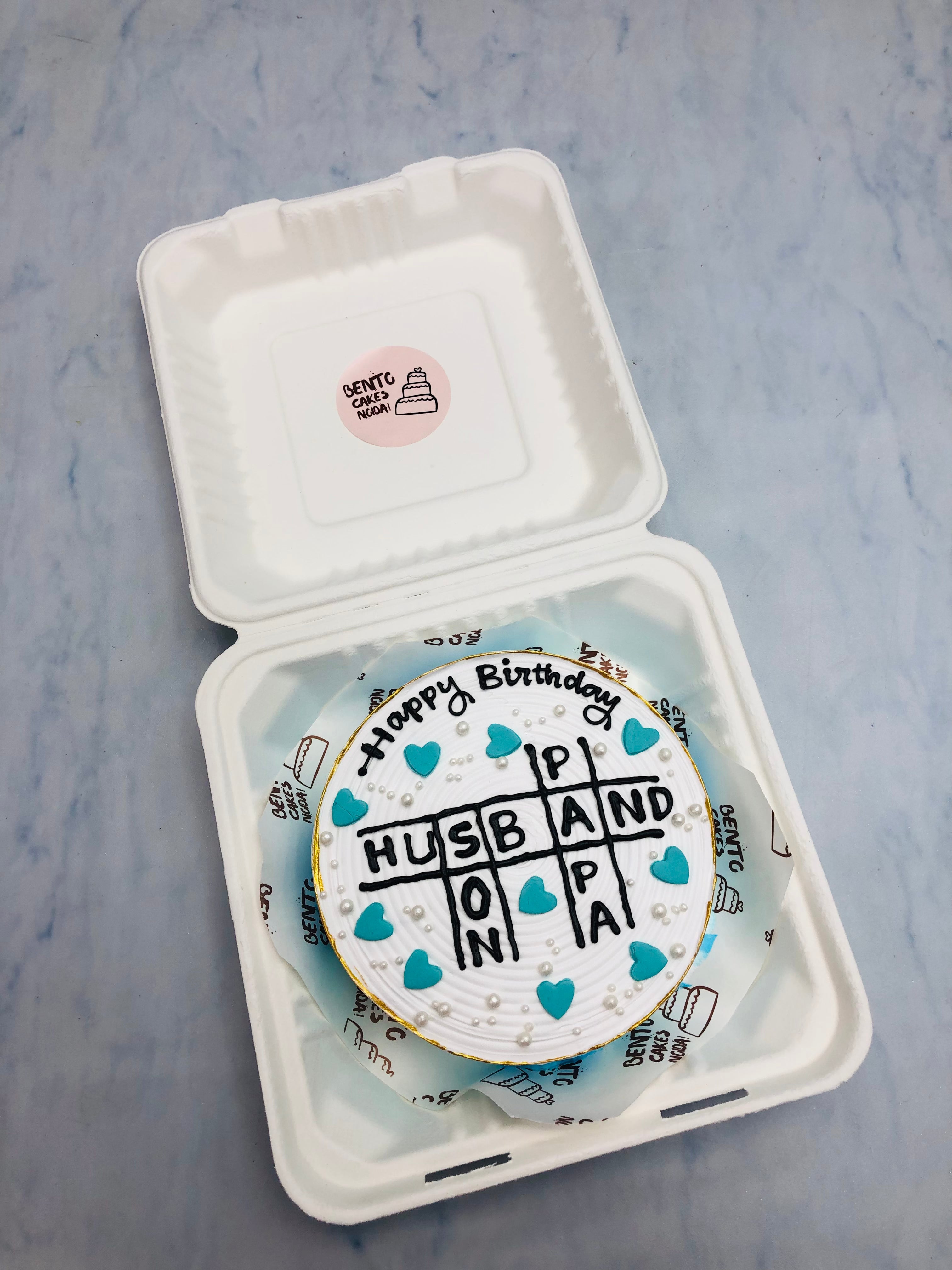 A aesthetic white bento cake with ombry design on top, and a puzzle design filled with HUSBAND, PAPA, SON for their birthday.