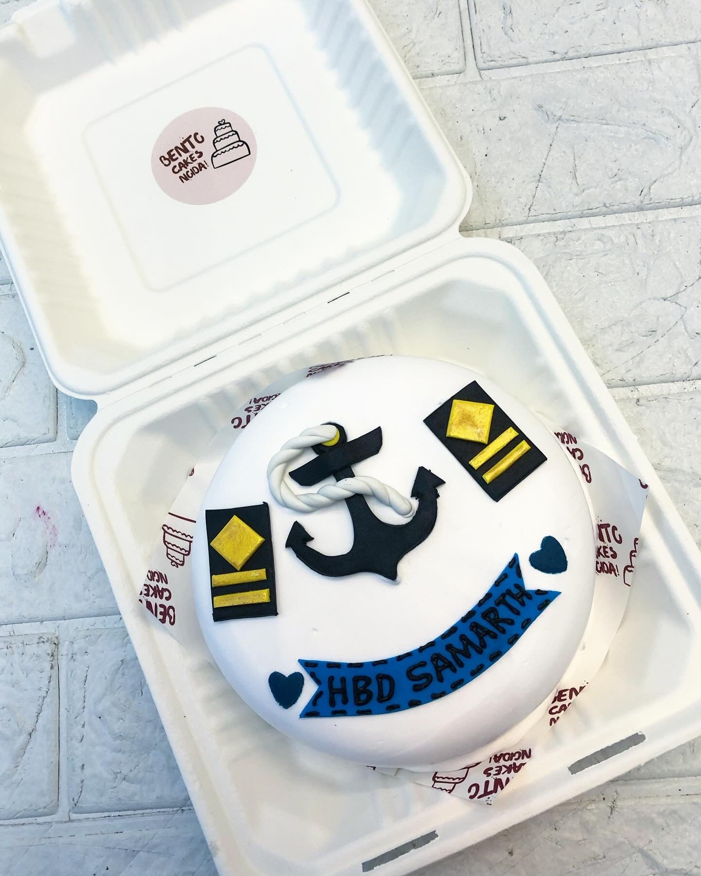 A white bento cake is designed with fondnt items for a merchant navy persons birthday.