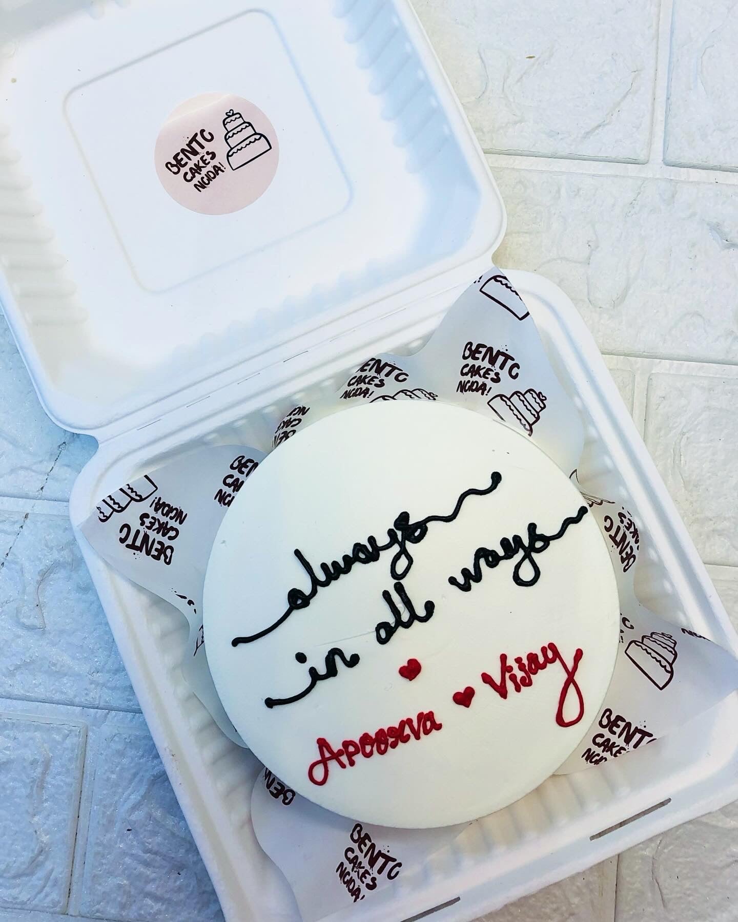 This Beautifully Designed white cake in a bento box having the text "Always In All Ways" written on top of the cake.