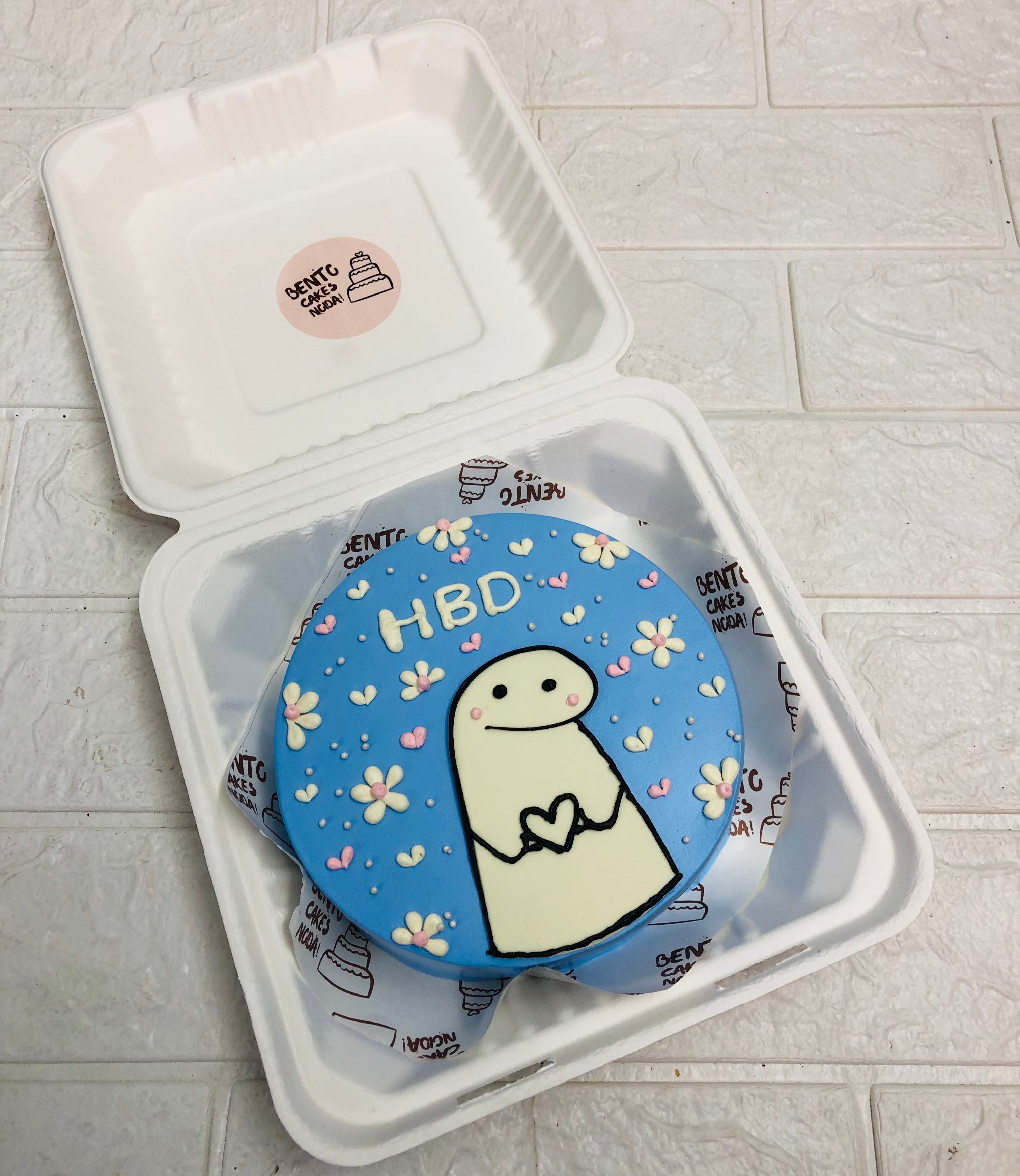 A round birthday cake with a blue icing decorated with a cute mimi illustration and floral patterns. The cake has "HBD" written on it.