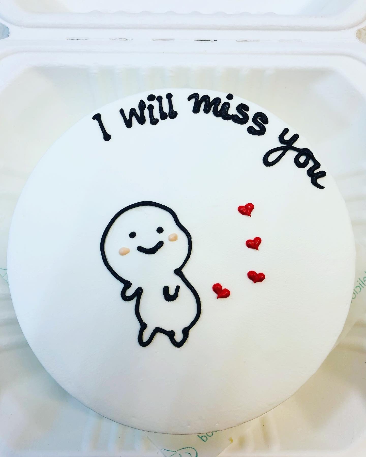 A white cake is decorated with a cute cartoon on it and some red colored heart designed around cartoon and a text of "I will miss you" written on it.