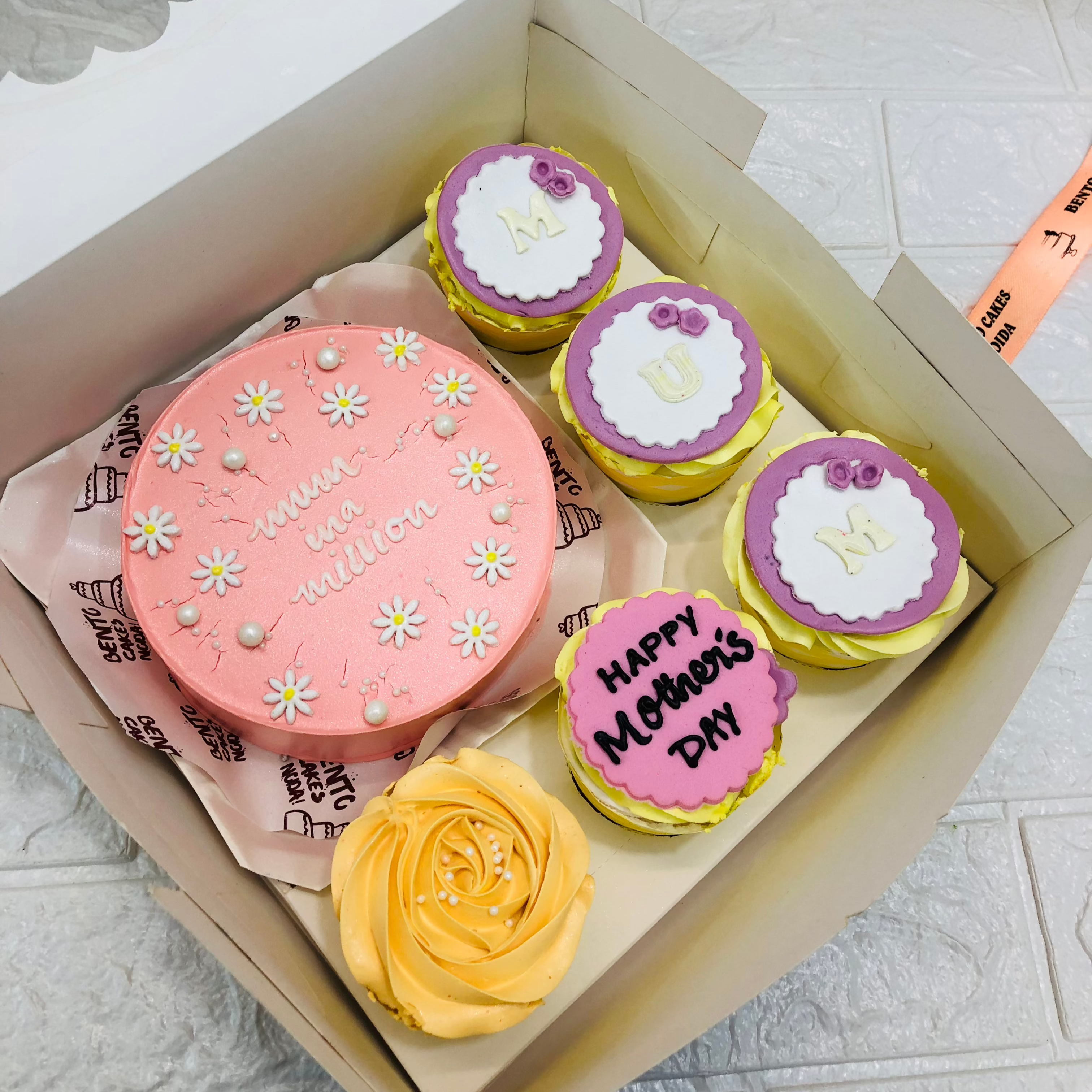A large bento box containing a cake and 5 cupakes. A light pink cake having floral design and cupcakes having floral and fondant designs.