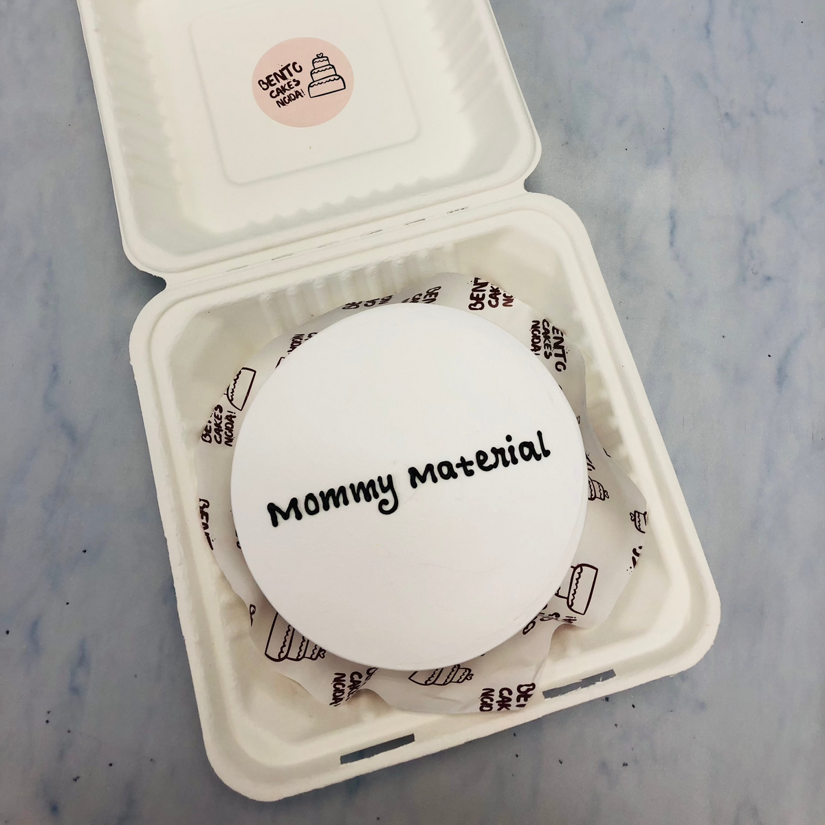 A white bento cake with a "Mommy Material" text in its center.