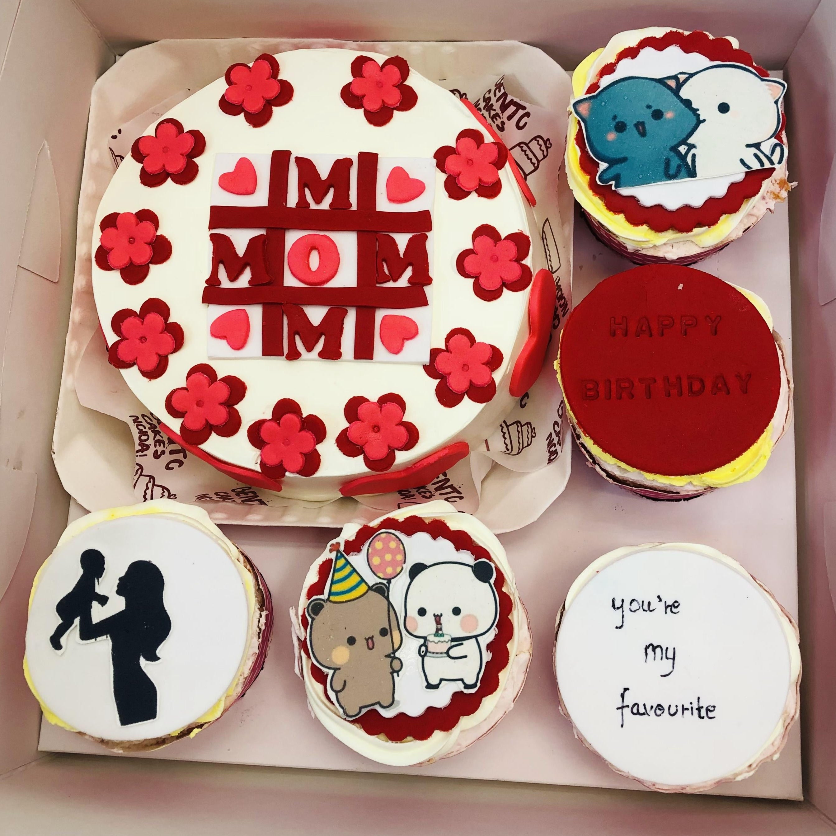 A decorative box containing a bento combo cake set. The main centerpiece is a round cake with white frosting, red flowers, and the text "MOM" in bold red letters. Surrounding the main cake are four smaller cakes, each with unique designs: one features a silhouette of a woman holding a child, another displays cartoon animals with party hats, one says "HAPPY BIRTHDAY," and the last one says "you're my favorite."