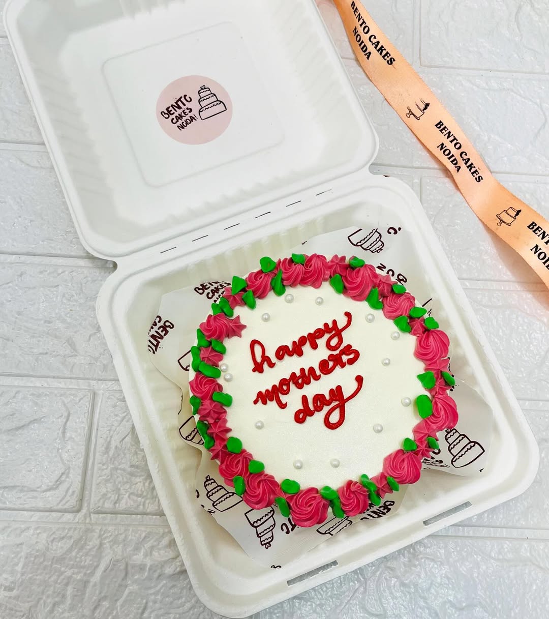 An offwhite cake with red floral design and  "happy mother's day" text written on it with red icing.