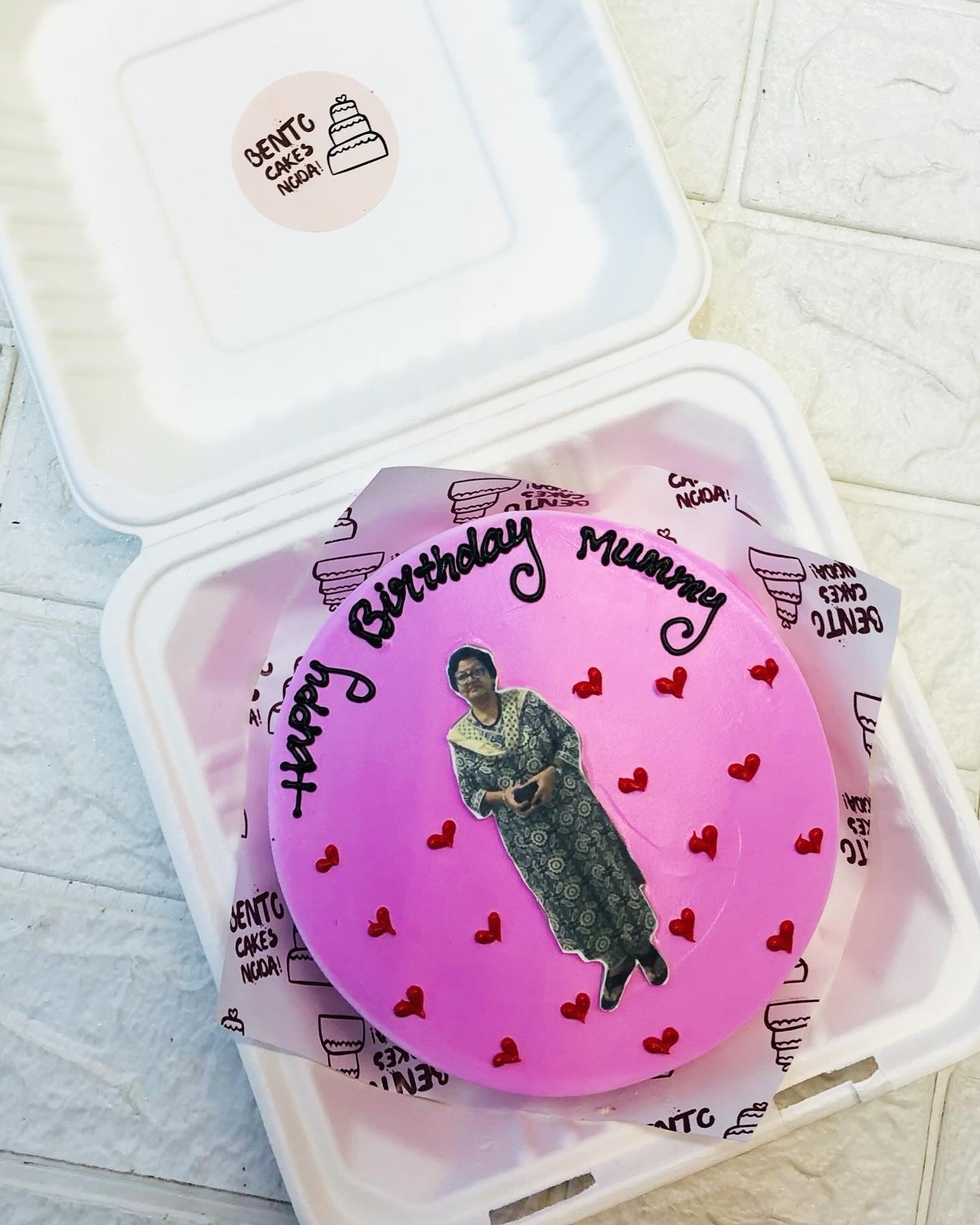 A pink frosting bento cake designed for mothers birthday with her photo on cake and decorated with red hearts design.