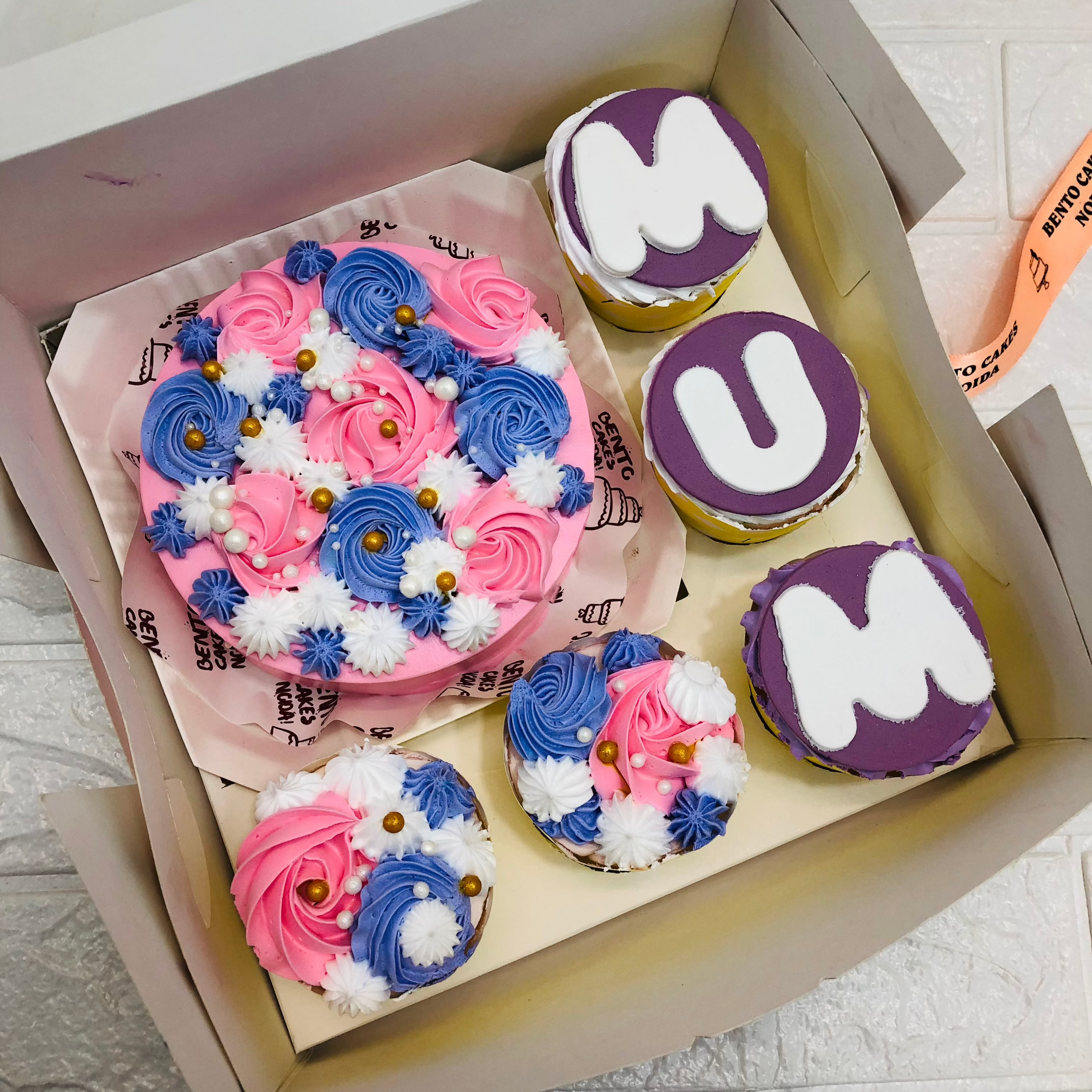 A large bento bo containing 1 cake and 5 cupcakes. An aesthetic pink floral design cake with 5 cupcakes having blue and purple and pink floral designs on it.