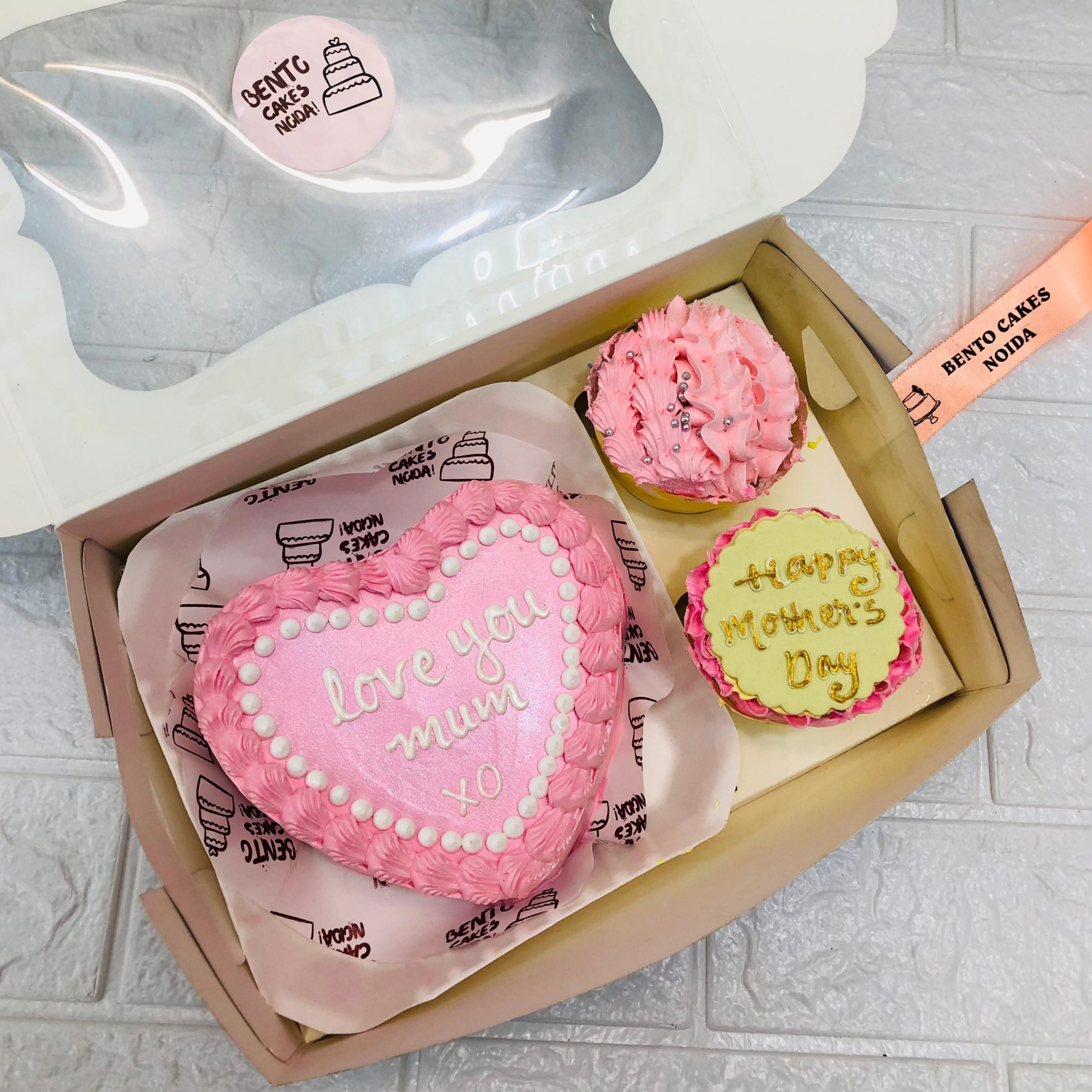 A mini bento combo having 1 cake and 2 cupcakes set. A pink color heart shape cake have and cupcakes having pink floral and yellow fondant design.