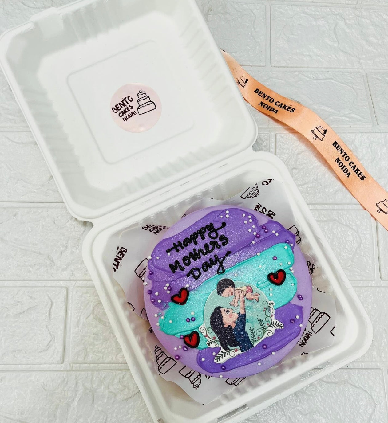 A purple bento cake having purple and blue shades on its top with a print of mom and baby for mothers day occasion.