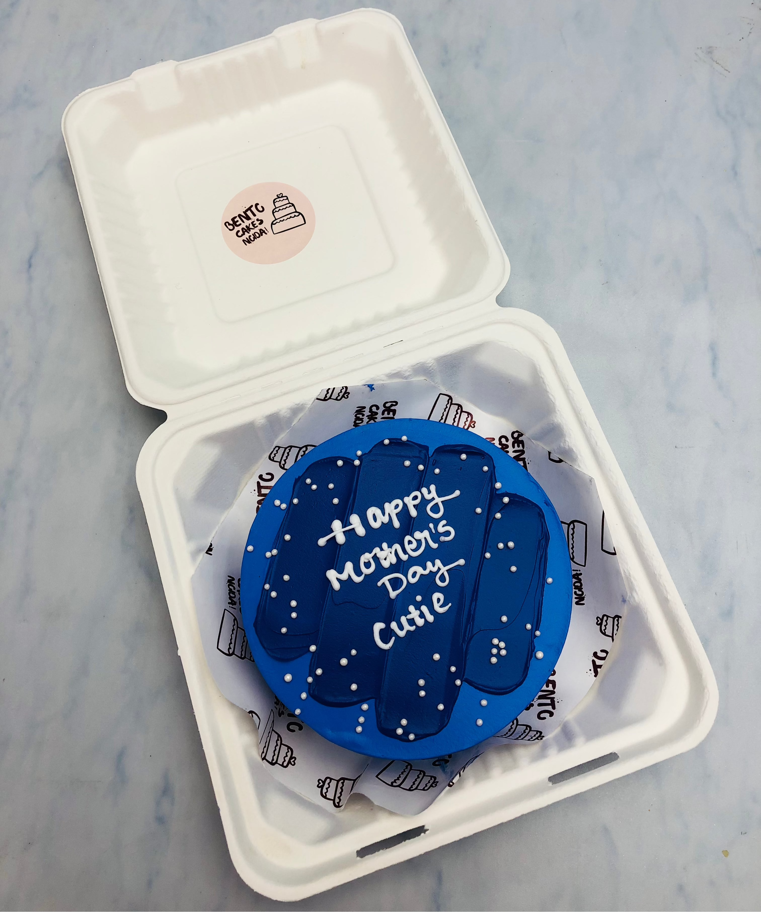 A blue bento cake with blue shades design and a text "Happy Mother's Day Cutie" written with white color.