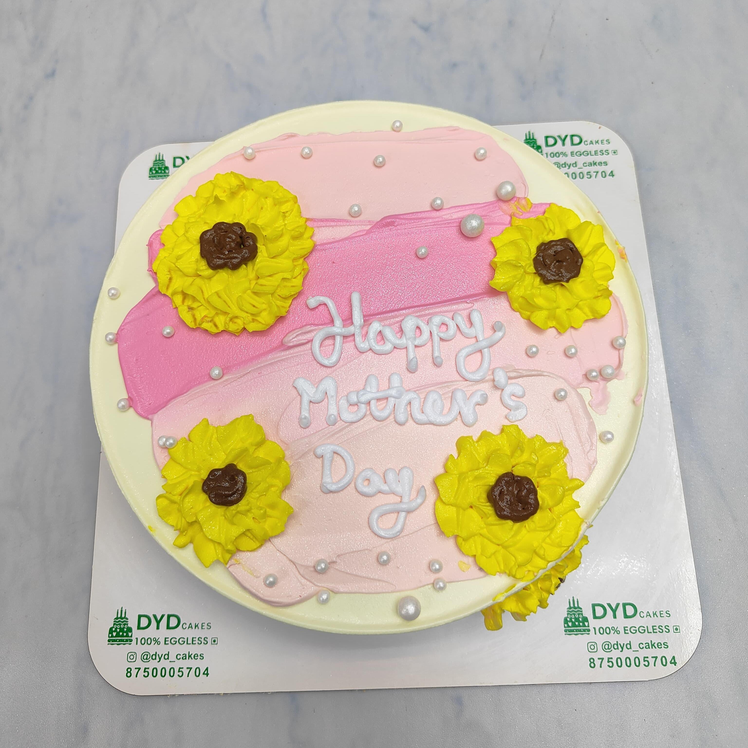 A white cake with pink shades and yellow florals designed on it with a "Happy Mother's Day" text.