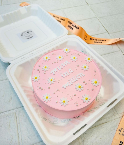 A light pink cake with pretty floral designs and decorated with hite sprinkles and a text "mum in a million" written with white icing on it.
