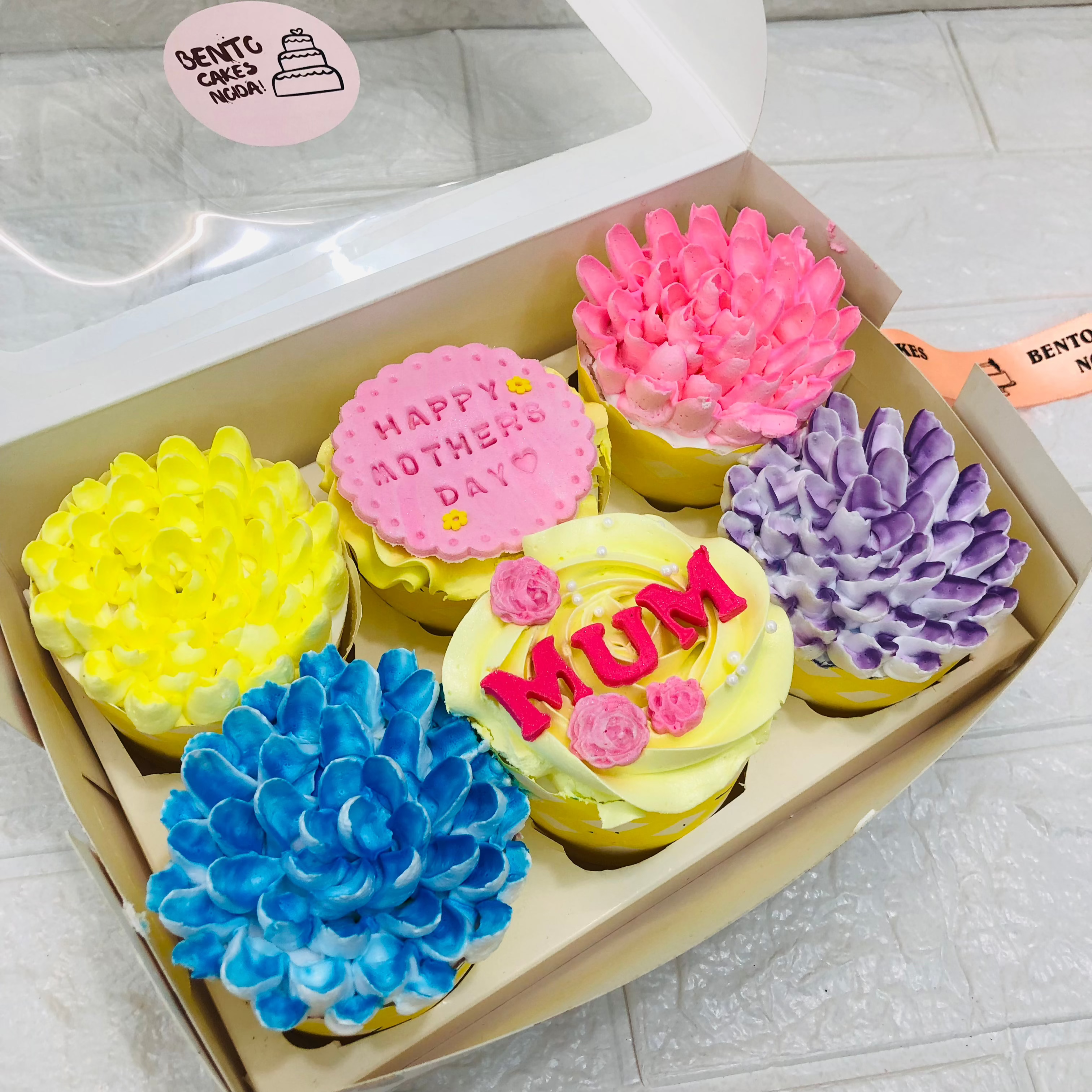 A box containing 6 cupcakes set in with 5 have different color floral design and one having fondant design for Mother's Day Occasion.