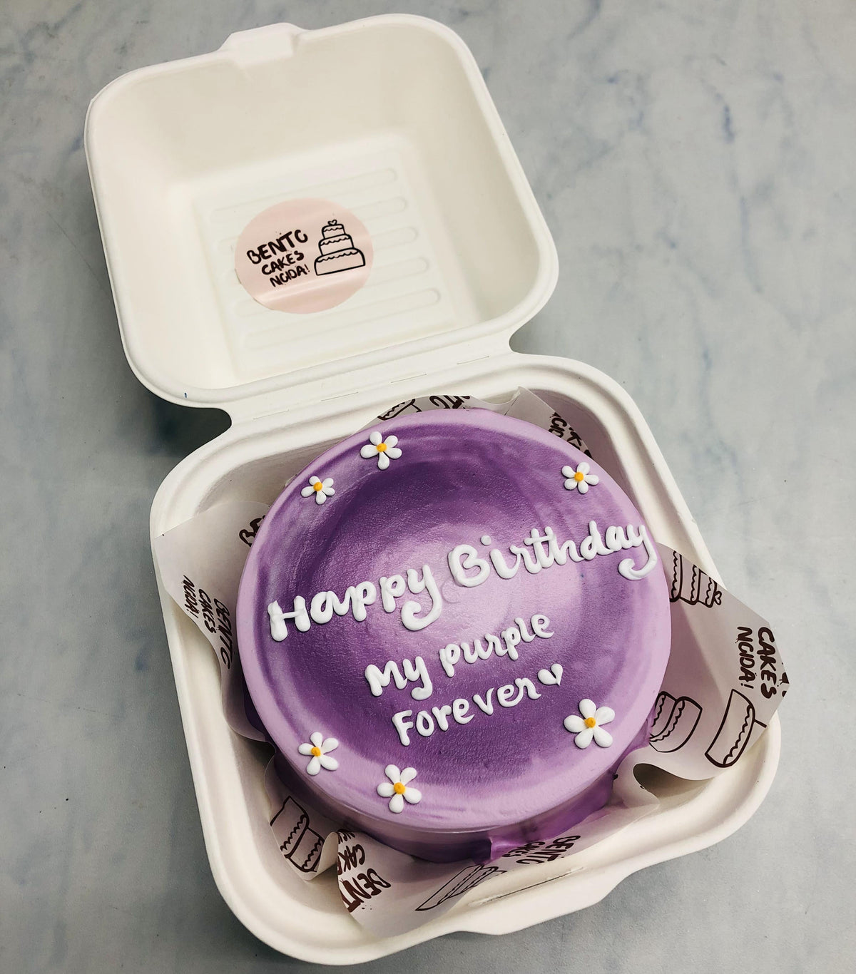 An aesthetic purple shades mini bento cake decorated with little white florals for birthday.