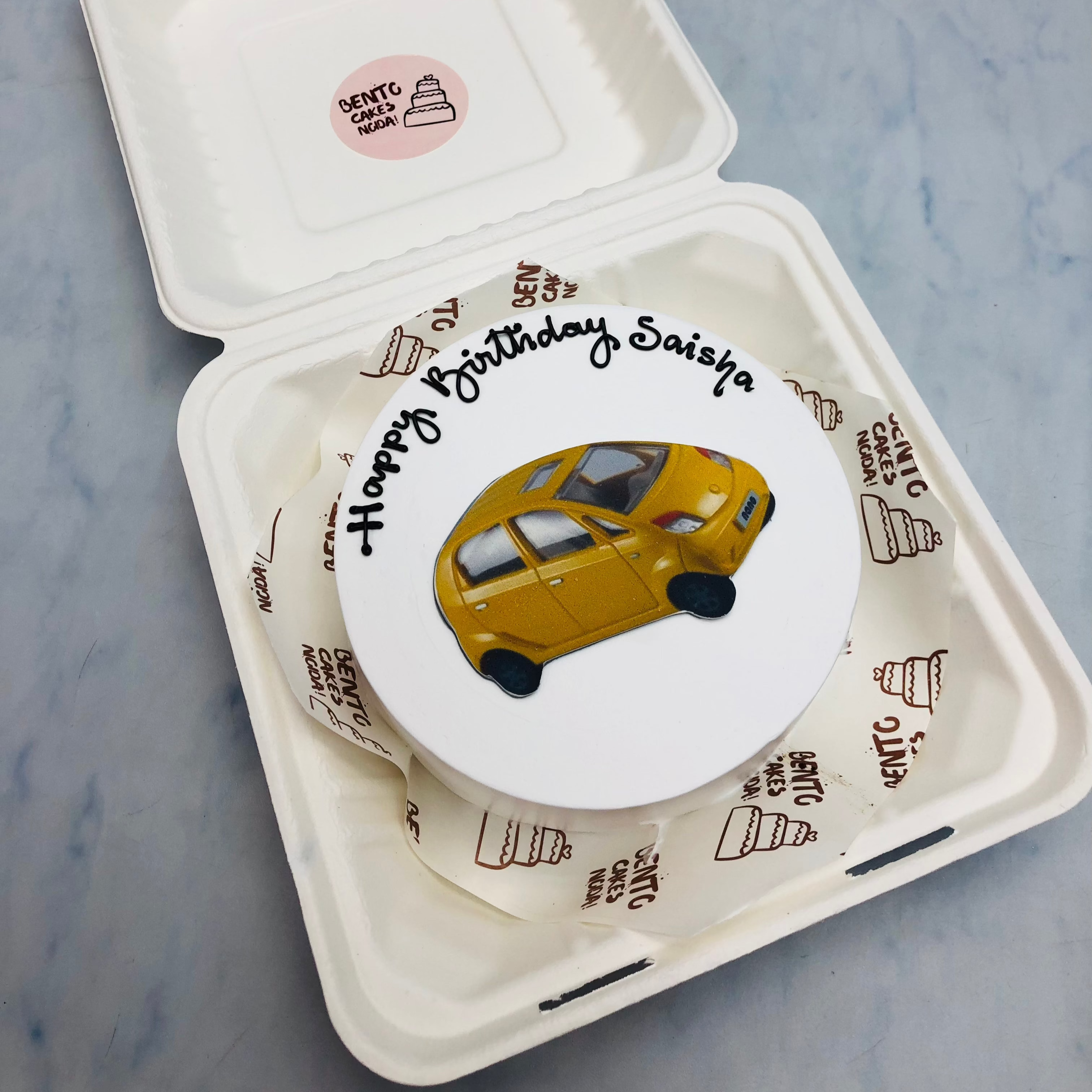 A white bento cake having a tata nano car print for birthday.