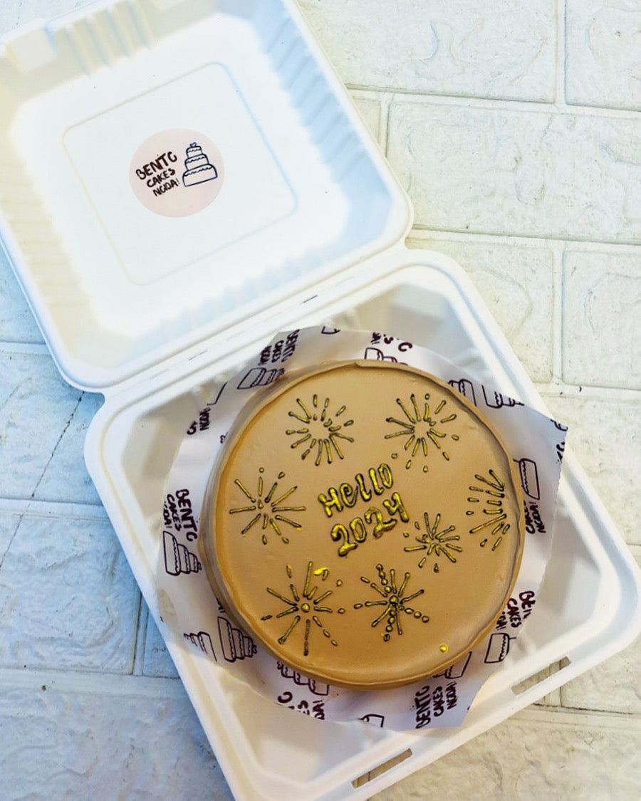 A golden brown bento cake with a sun type design on the top for welcoming new year.