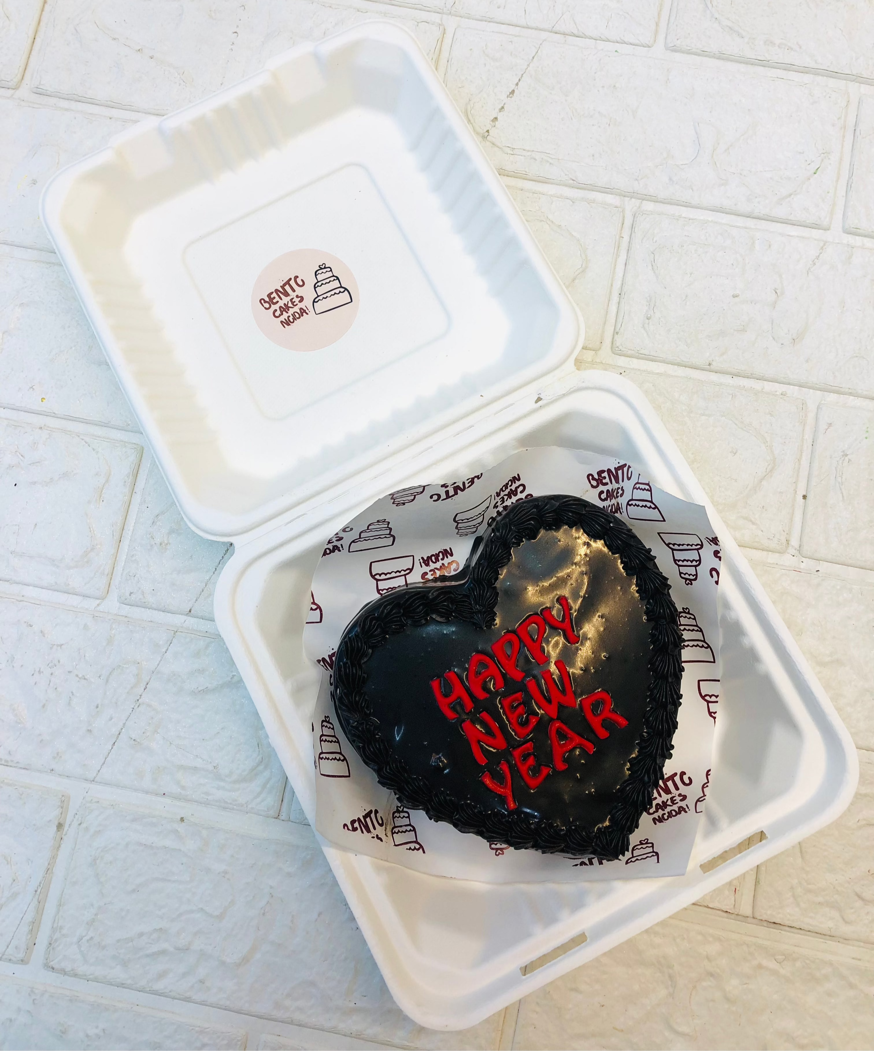 A dark chocolate heart shape cake with black borders design and a text "Happy New Year" written with red piping.