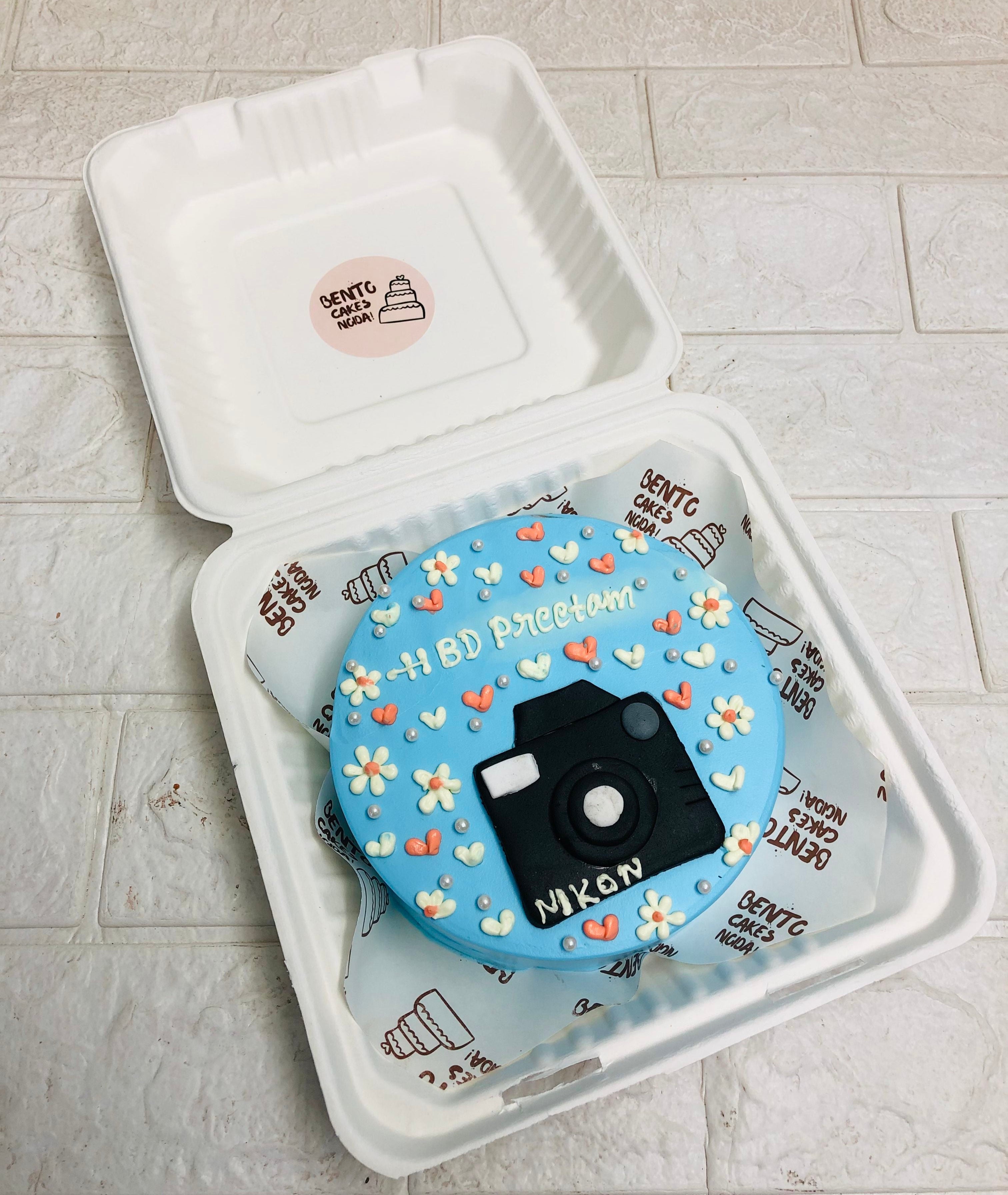 A floral blue bento cake is designed with nikon camera for birthday.